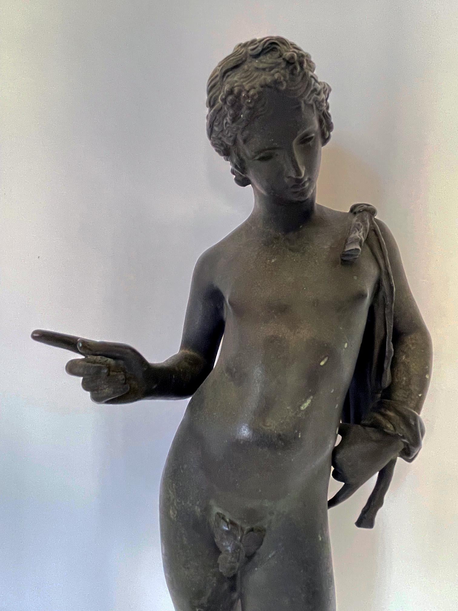 the youth in contrapposto pose with his right arm raised with a goat-skin slung over his left shoulder, his legs slightly apart and wearing sandals. leaning on one hip and looking downwards at his reflection; the original figure discovered in