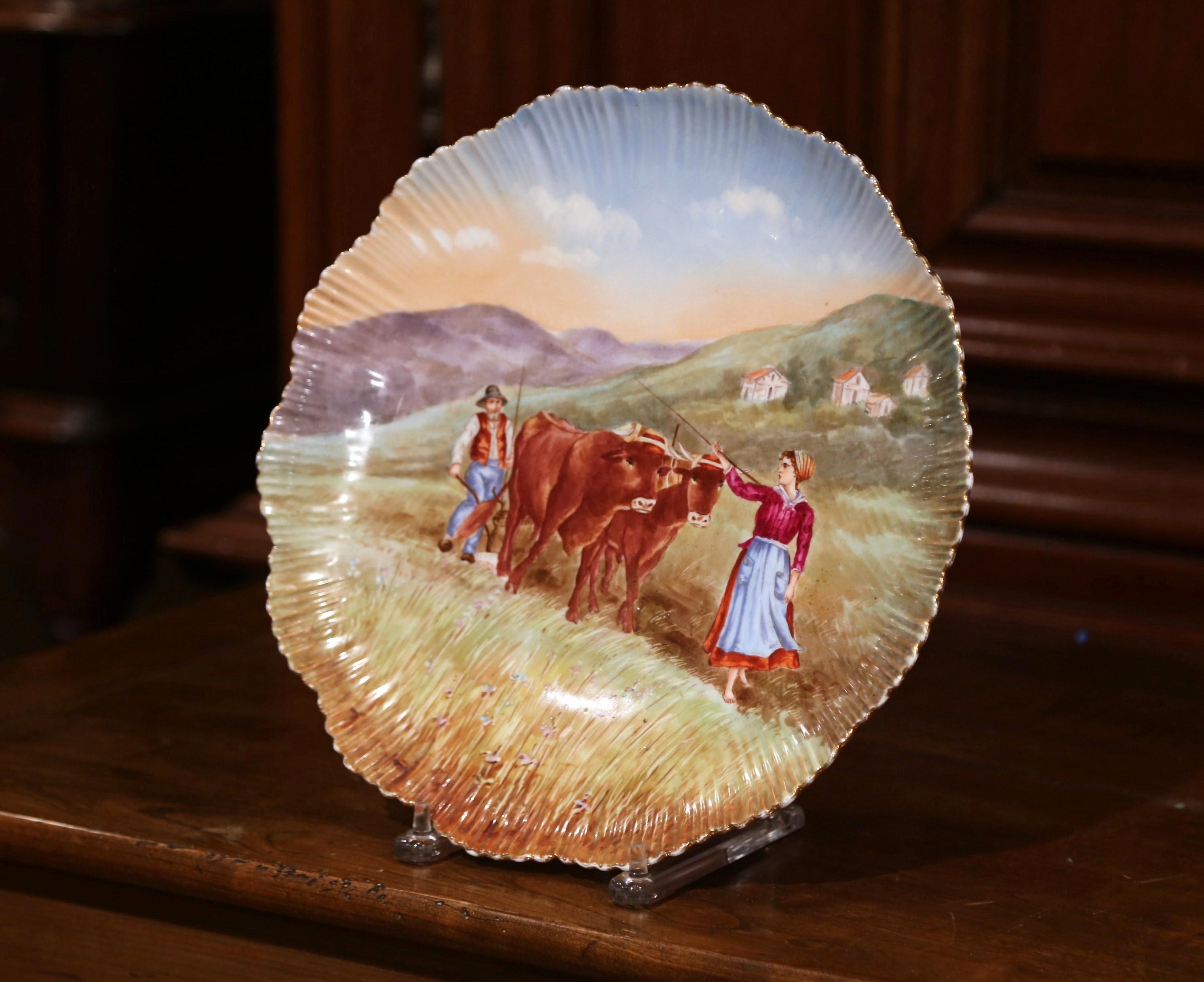This large antique platter was sculpted in northern France, circa 1880. The hand painted landscape scene features a peasant couple plowing a field with a pair of cows pulling. The decorative porcelain plate has a scalloped edge and a rich palette of