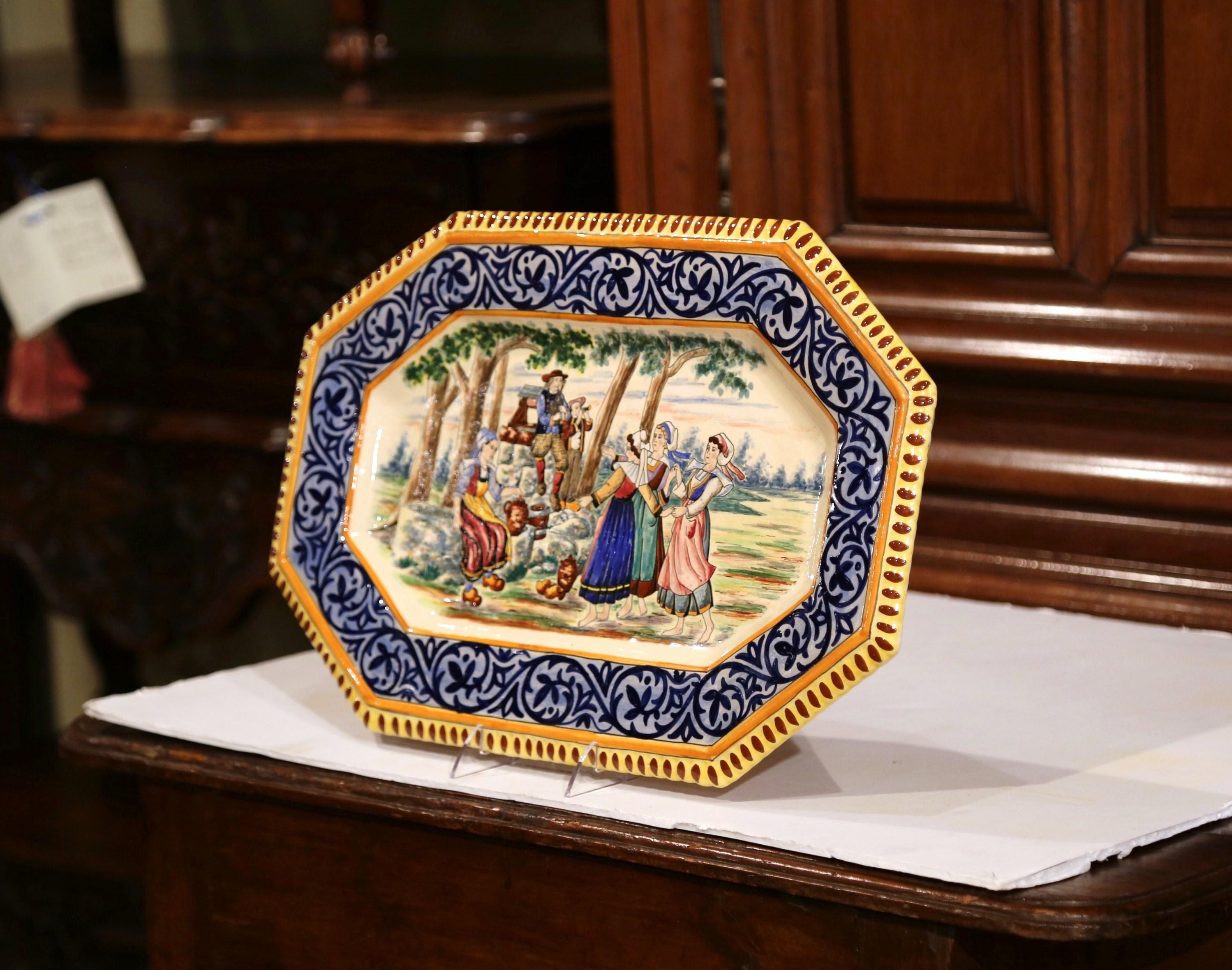 This large antique and colorful wall plate was created in Brittany, circa 1870. Hand painted in the blue and yellow palette and signed on the back HB Quimper, the ceramic platter has a large blue and yellow border and features Briton people in
