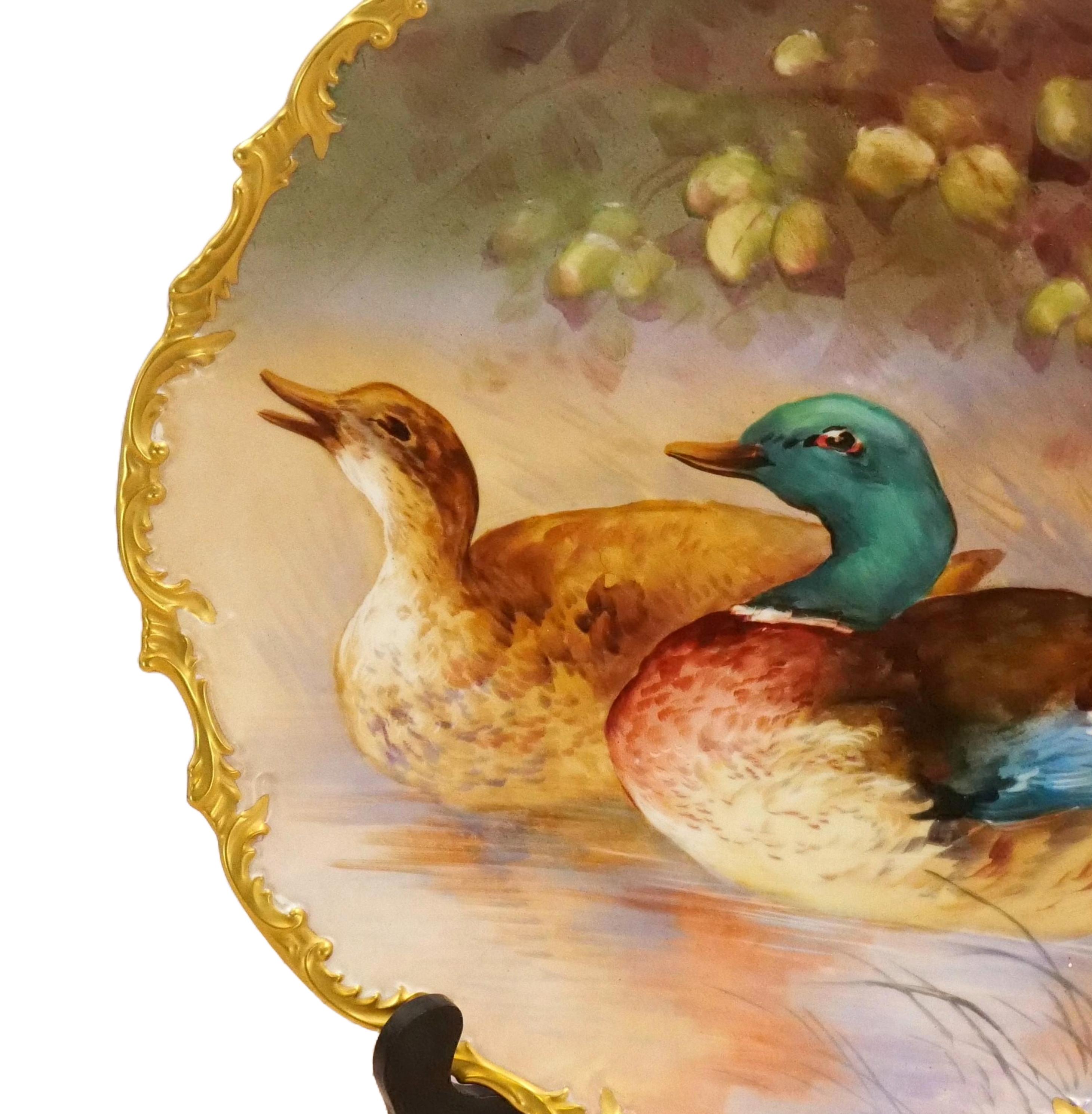 Presenting a large 19th century French Limoges wall art painted decorative plate, a captivating showcase of artistry and elegance. This remarkable piece features a beautifully hand-painted scene depicting two colorful ducks gracefully swimming in