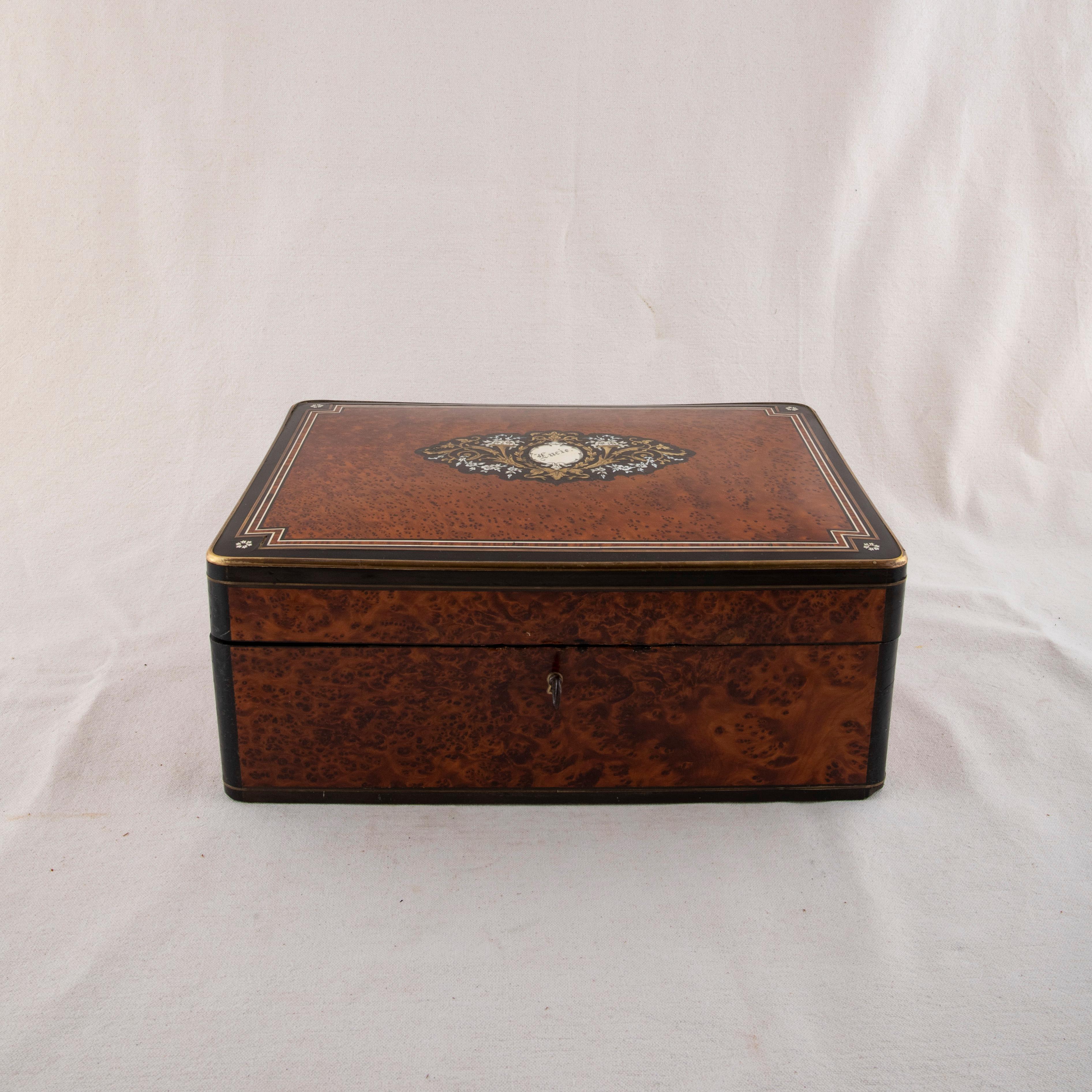 This large mid nineteenth century marquetry box from the Napoleon III period features a burl thuya wood field surrounded by a concentric border of intricately inlaid ebonized pearwood, ivory, and rosewood. An ivory cartouche in the center of the lid