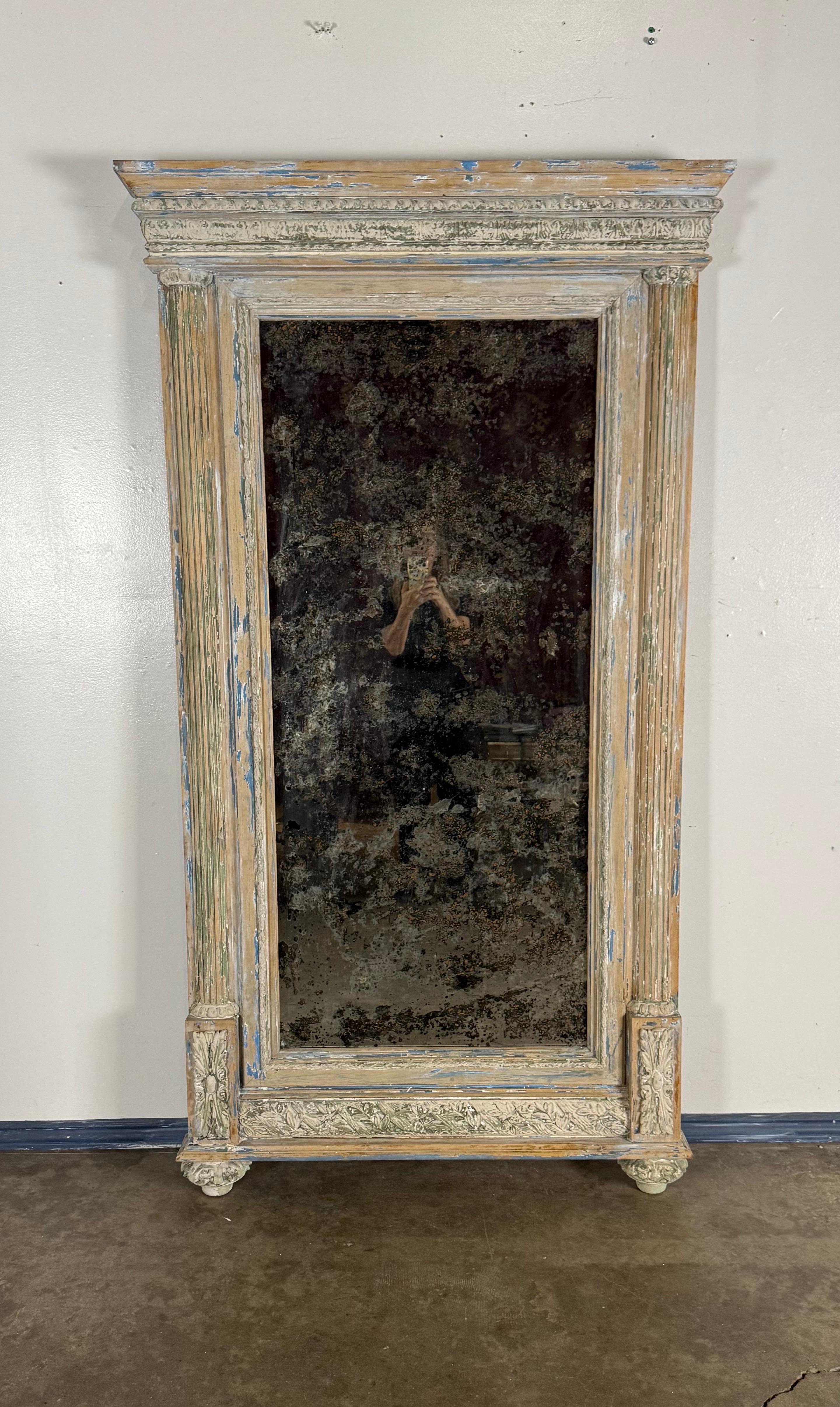 A magnificent French trumeau mirror in the Neoclassical style, featuring an elaborately carved frame with fluted pilasters, acanthus detailing, and a bold cornice top. The surface retains its original multi-layered painted finish, beautifully