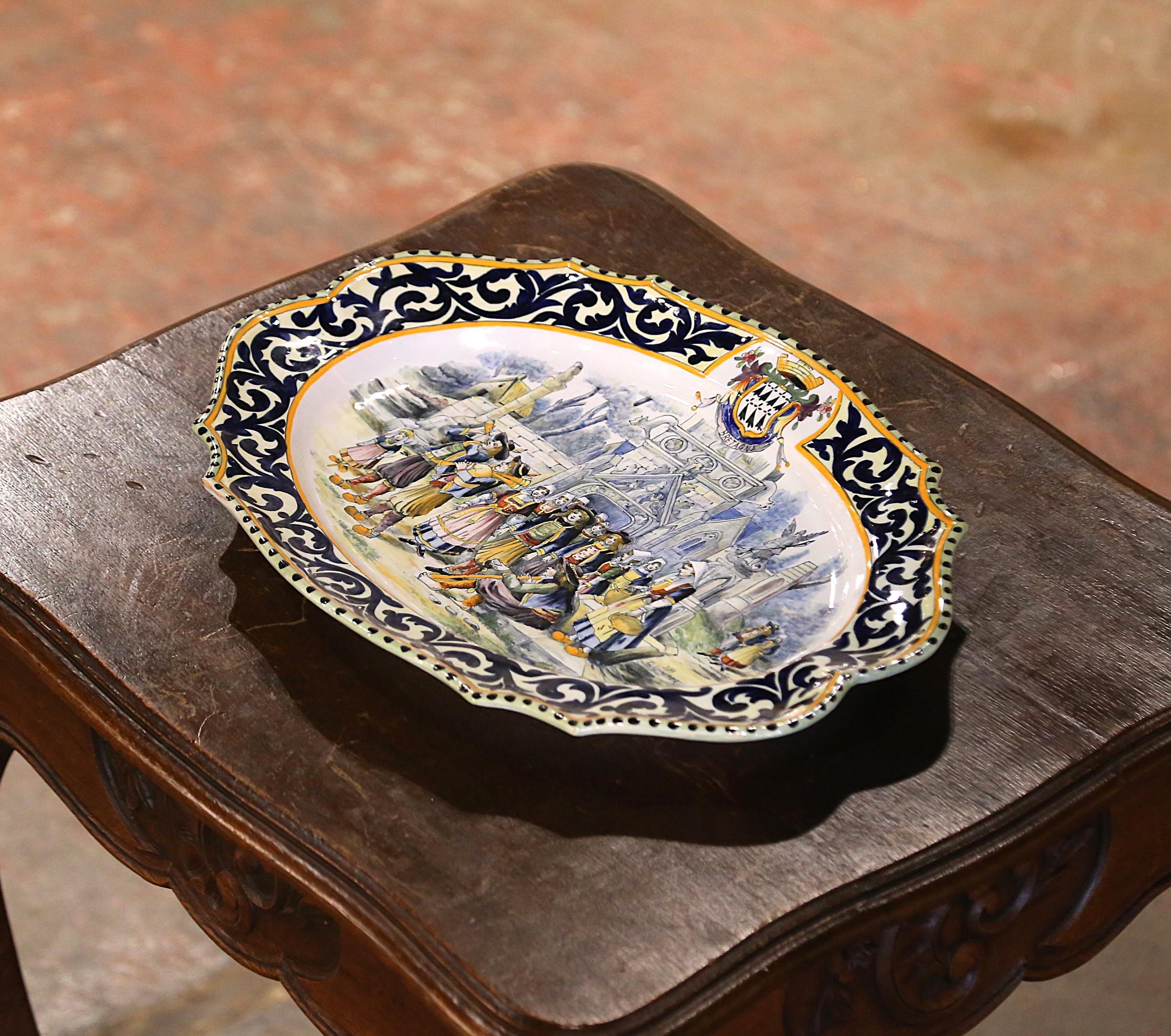 Décorez un mur de cuisine ou une étagère avec cet important plateau ancien. Créée en Bretagne (France) vers 1895, cette grande assiette en céramique peinte à la main représente une scène traditionnelle avec des Bretons en costumes, se rassemblant