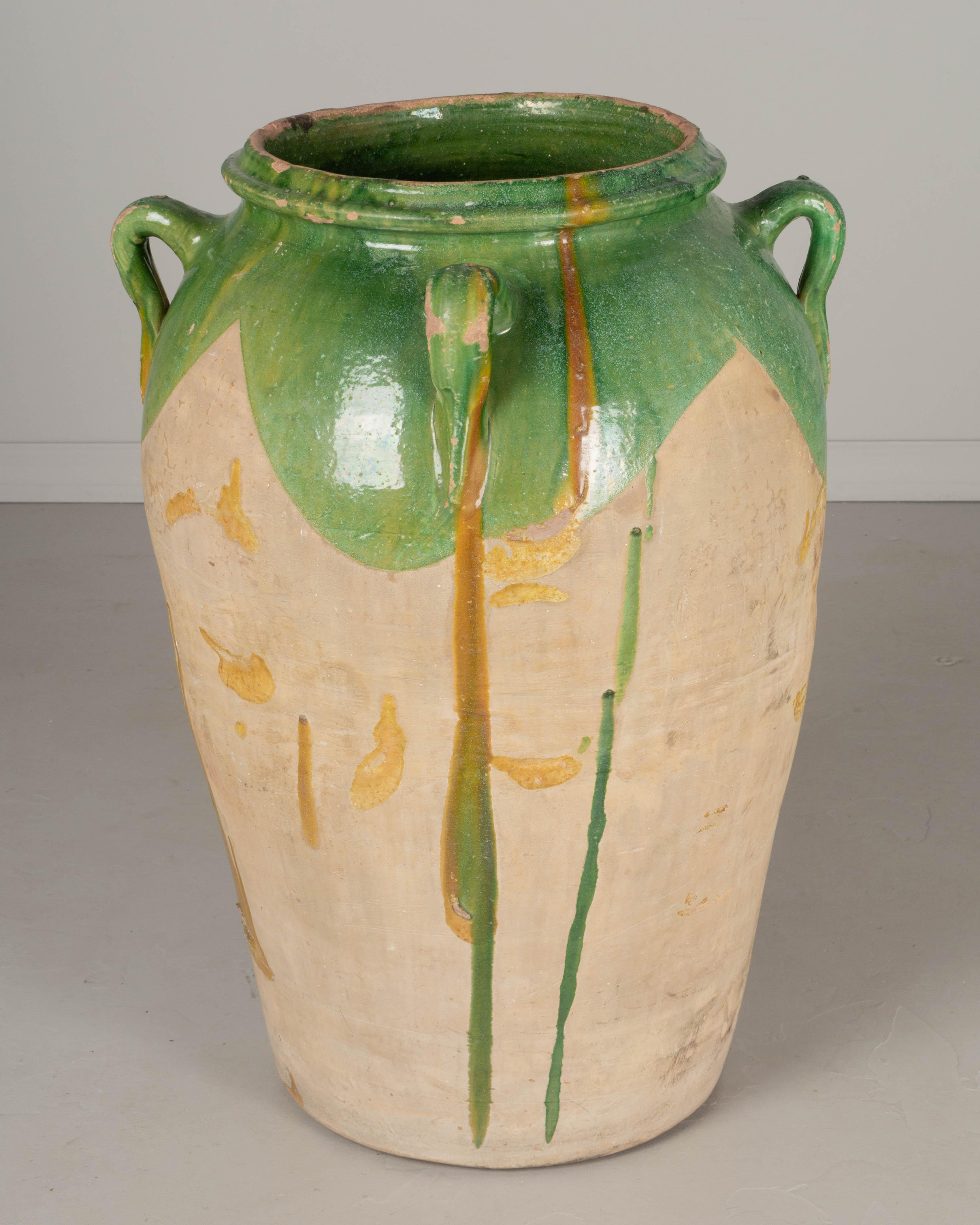 A large early 20th Century terracotta pottery jar from the Southwest of France. Classic urn shape with four small handles. Green glazed top and unglazed body with green and yellow ochre drips. A beautiful garden ornament, fountain, or planter,