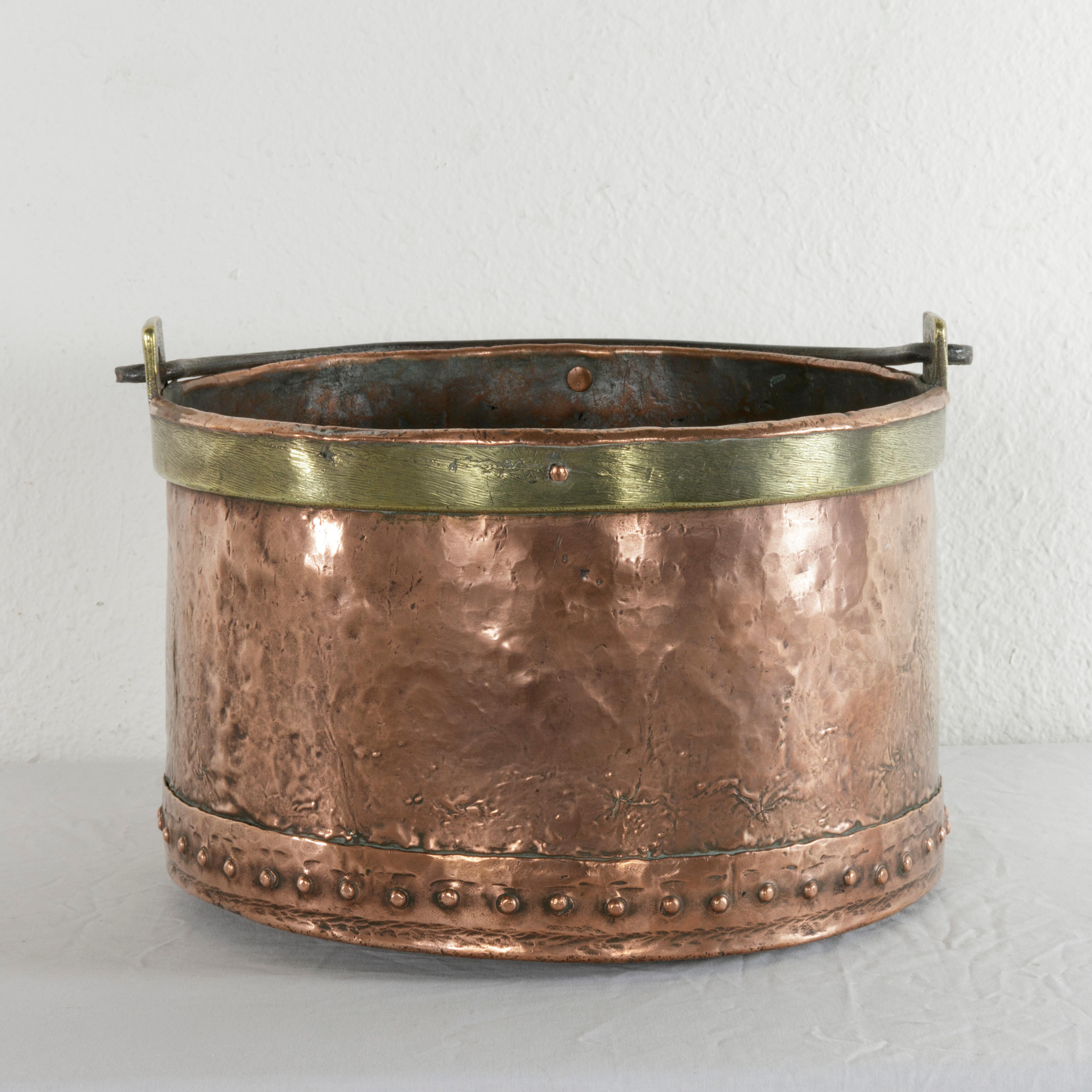 This large late 19th century copper cauldron features brass banding around the top and a hand-forged iron handle. The hand-hammered facade of the piece is joined to the bottom with copper rivets, adding to its aesthetic appeal. Ideal as a planter or