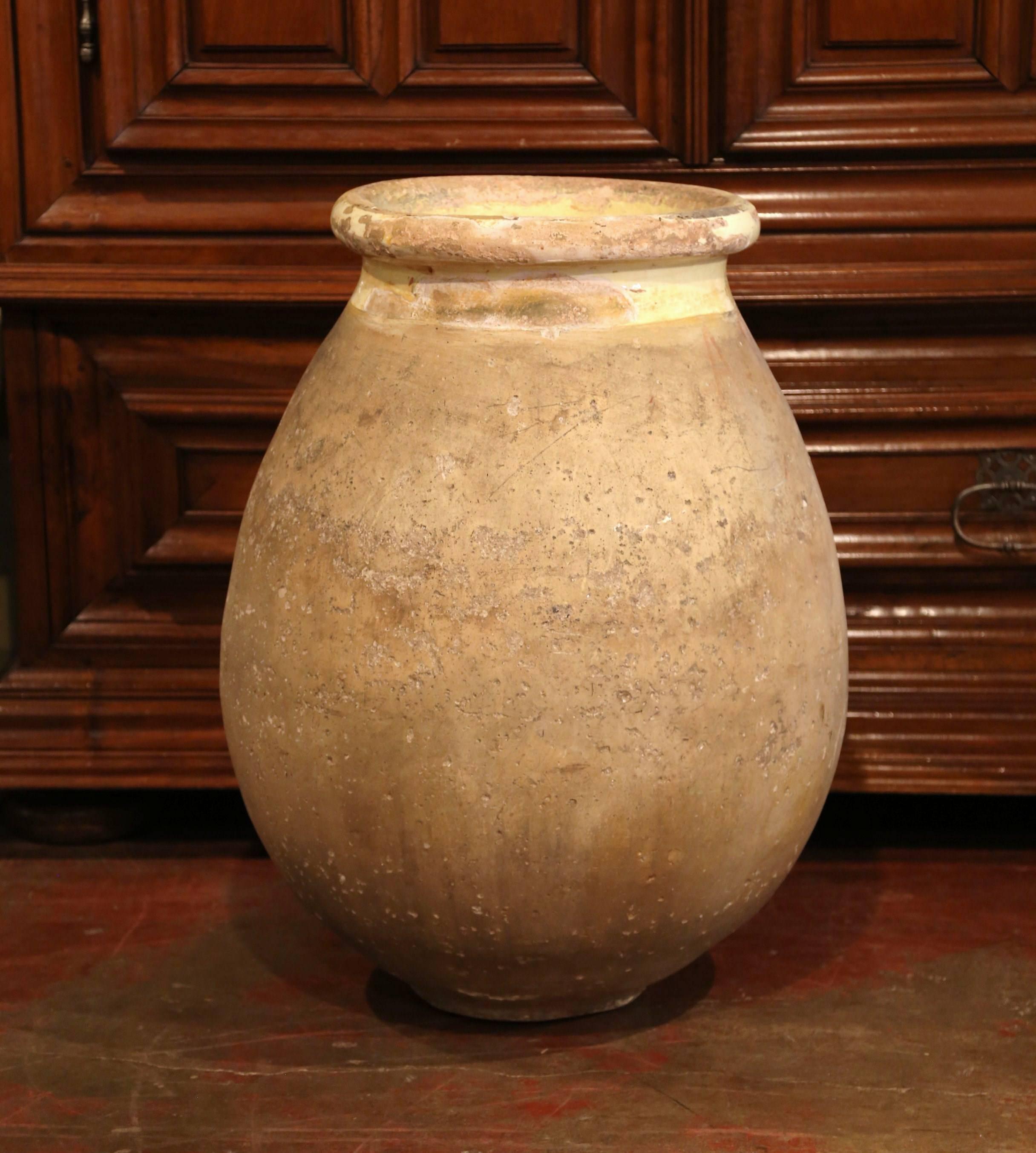 This large, antique earthenware olive jar was created in Southern France, circa 1870. Made of blond clay and neutral in color, the terracotta has a traditional round shape; the pot features a yellow glaze around the neck and trim, and a natural