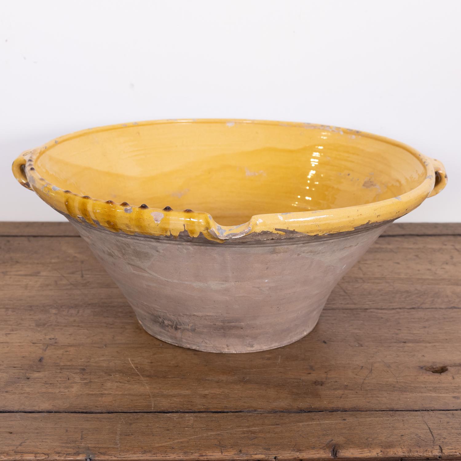 A large 19th century French tian bowl complete with both handles and pouring spout having an unglazed pale terracotta exterior and a bright yellow glaze to the interior and lip, circa 1880s. Earthernware tian bowls like this are considered