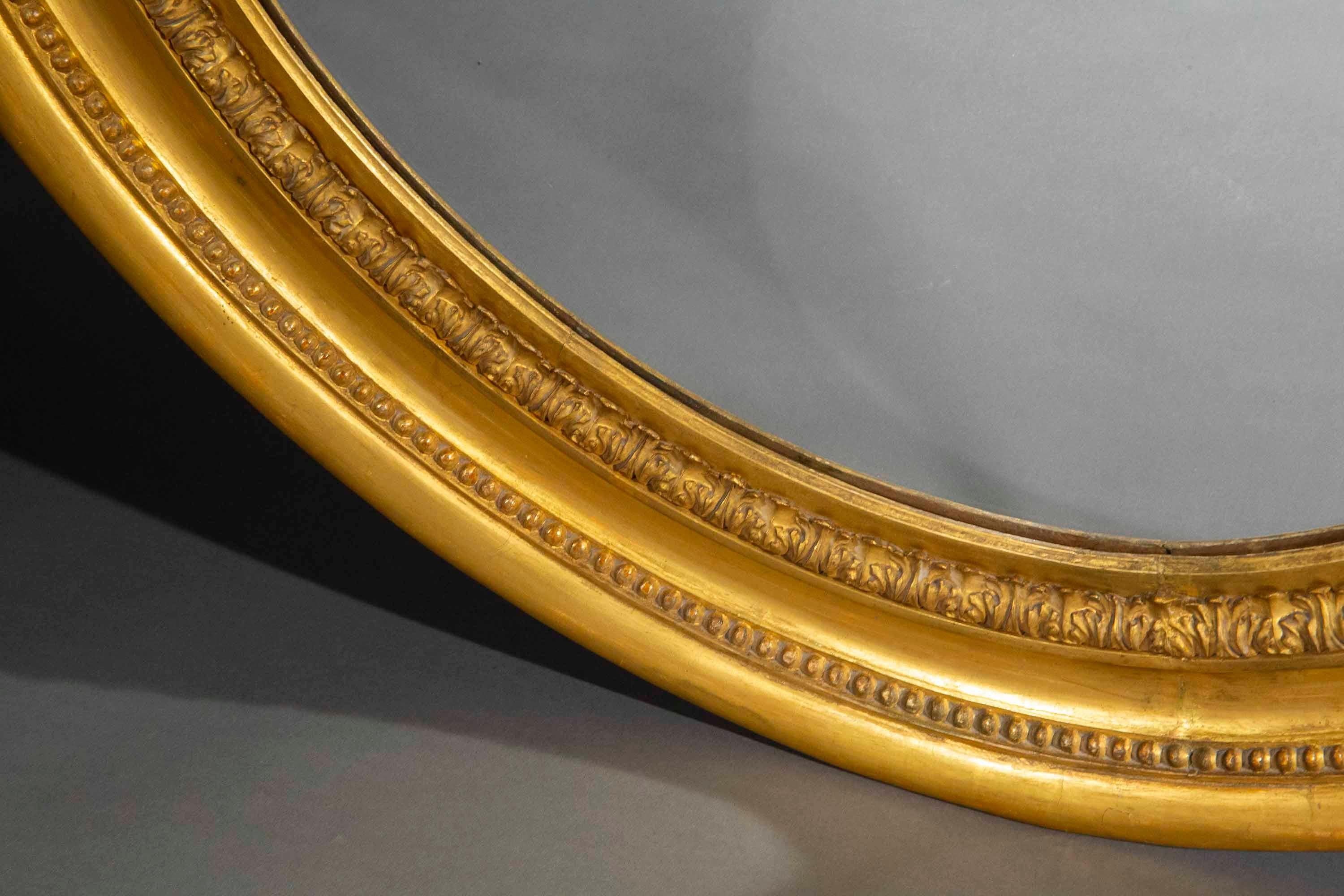 Rare et très élégant miroir mural ovale en bois doré de grandes proportions, conçu dans le style des frères Adams, pionniers du style néoclassique à la fin du XVIIIe siècle en Grande-Bretagne. Datant de la fin de l'époque géorgienne et du début de