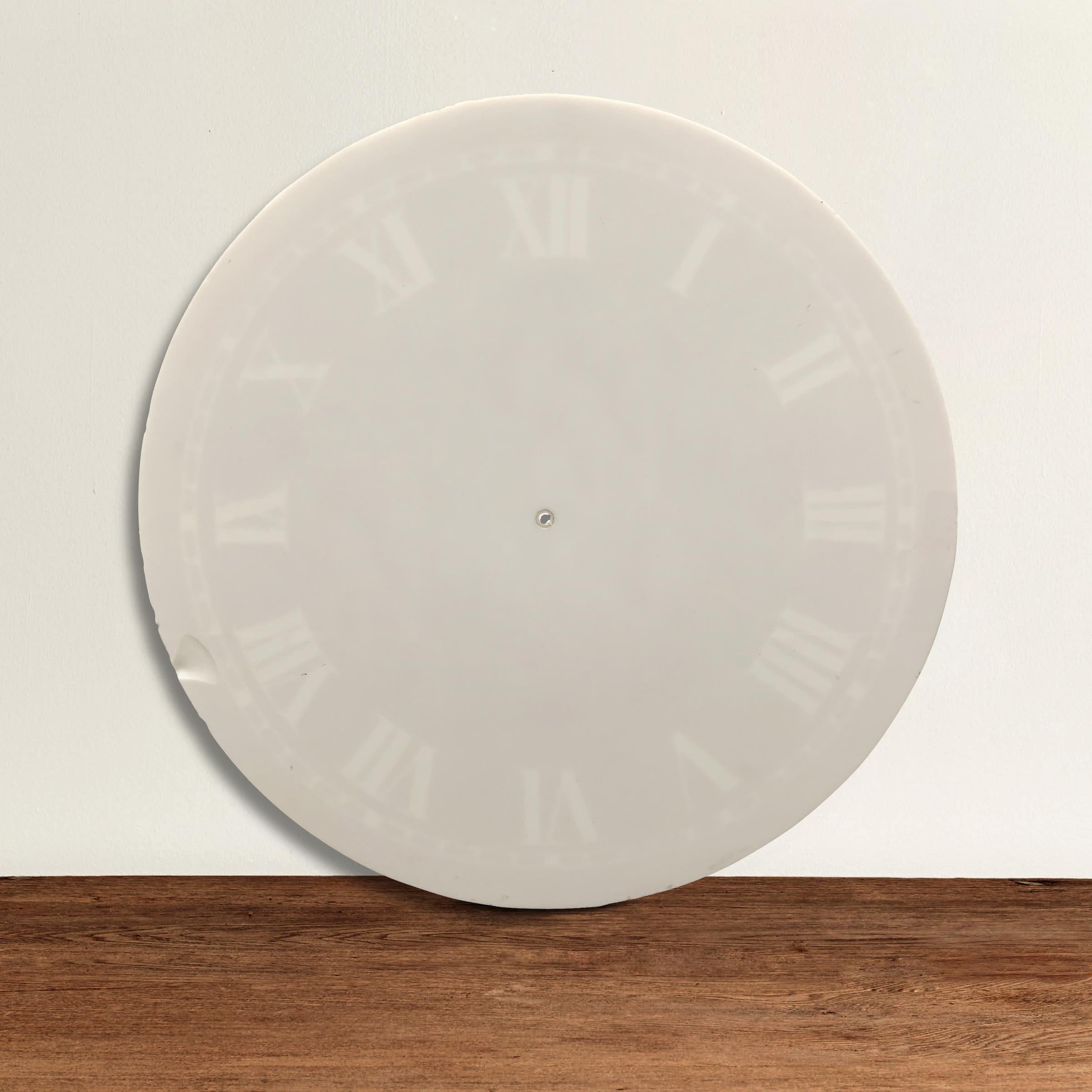 A large 19th century American milk glass clock face with faded Roman numerals around the perimeter. The numbers were originally applied to the surface of the glass and have left a shadow impression. The mineral, manganese, used to be added to glass