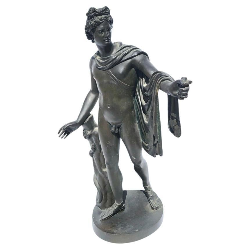 19th Century Grand Tour Bronze Sculpture of Apollo Belvedere. The Greek god Apollo is depicted as a standing archer having just shot an arrow. Apollo appears semi-clad with drapery folded over left arm, beside a rustic tree stump entwined by a
