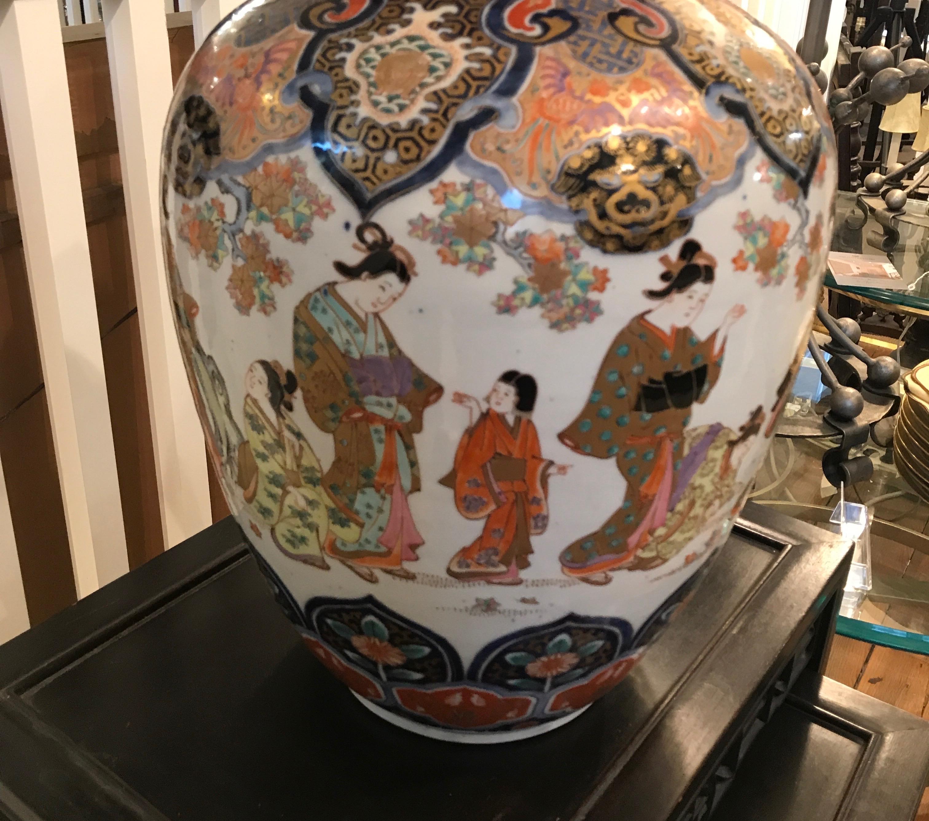 A remarkable hand painted Japanese porcelain Imari vase. Classic iron red and cobalt blue on a white porcelain background. Elegant Japanese figures painted all around the center portion with intricate detailed top and bottom with gilt highlights.