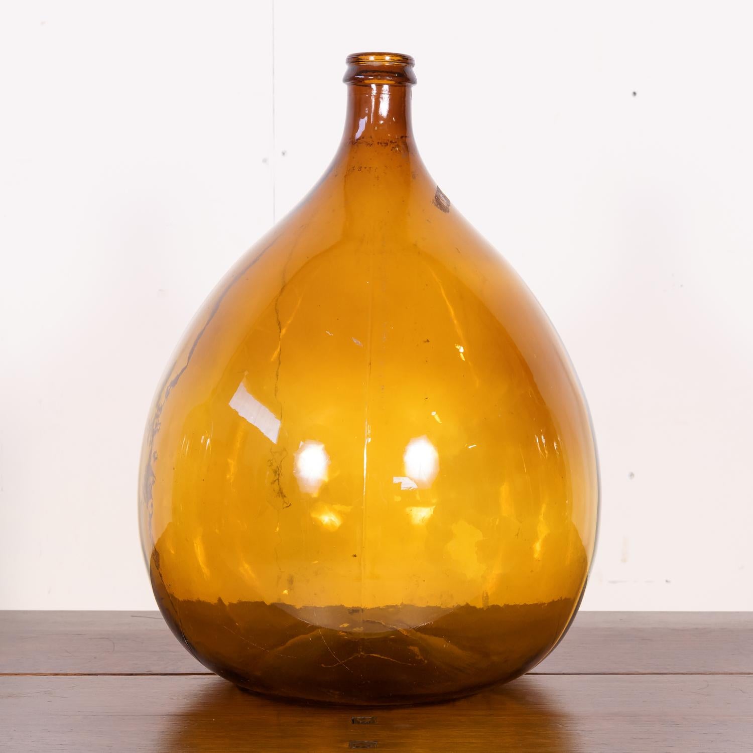 A large 19th century French hand blown glass demijohn or Dame Jeanne bottle, circa 1890s. This beautifully bulbous shaped and bright amber colored glass bottle has visible bubbles and no seams, indicating it was hand blown rather than made with a