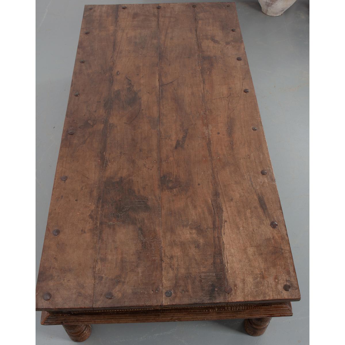 A large Indian teak low table – purchased in France – from the late 19th Century. It has a rich finish and beautiful nailhead trim around the top perimeter of the table. The apron has a nice carved banding wrapping the table and metal brackets at