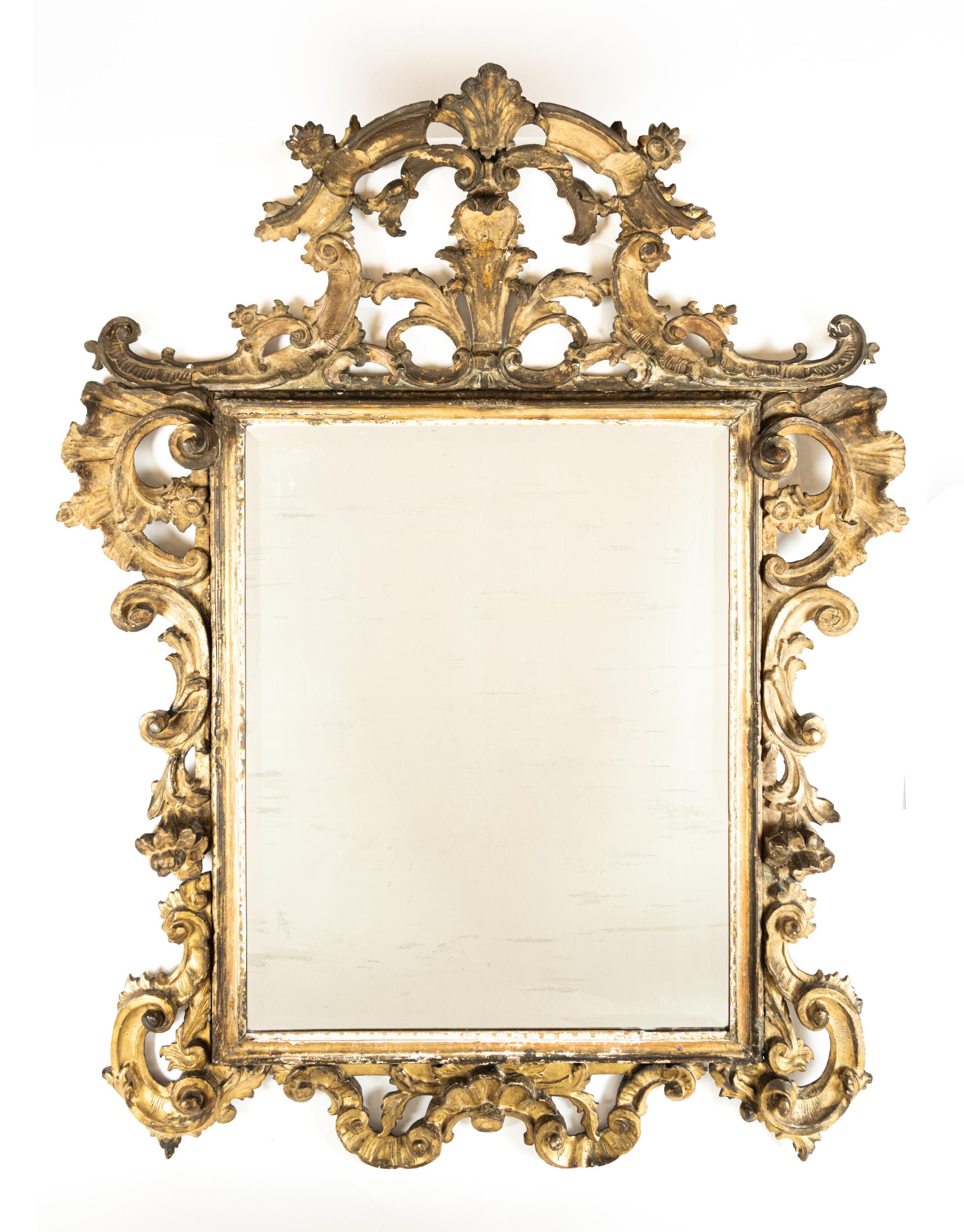 A large Italian Rococo carved gilt wood mirror. Having a rectangular vertical glass frame with a hand carved crested top formed by leaf, floral, and scroll motifs. Featuring pierced carving, creating a symmetrical frame, and a pleasant overall