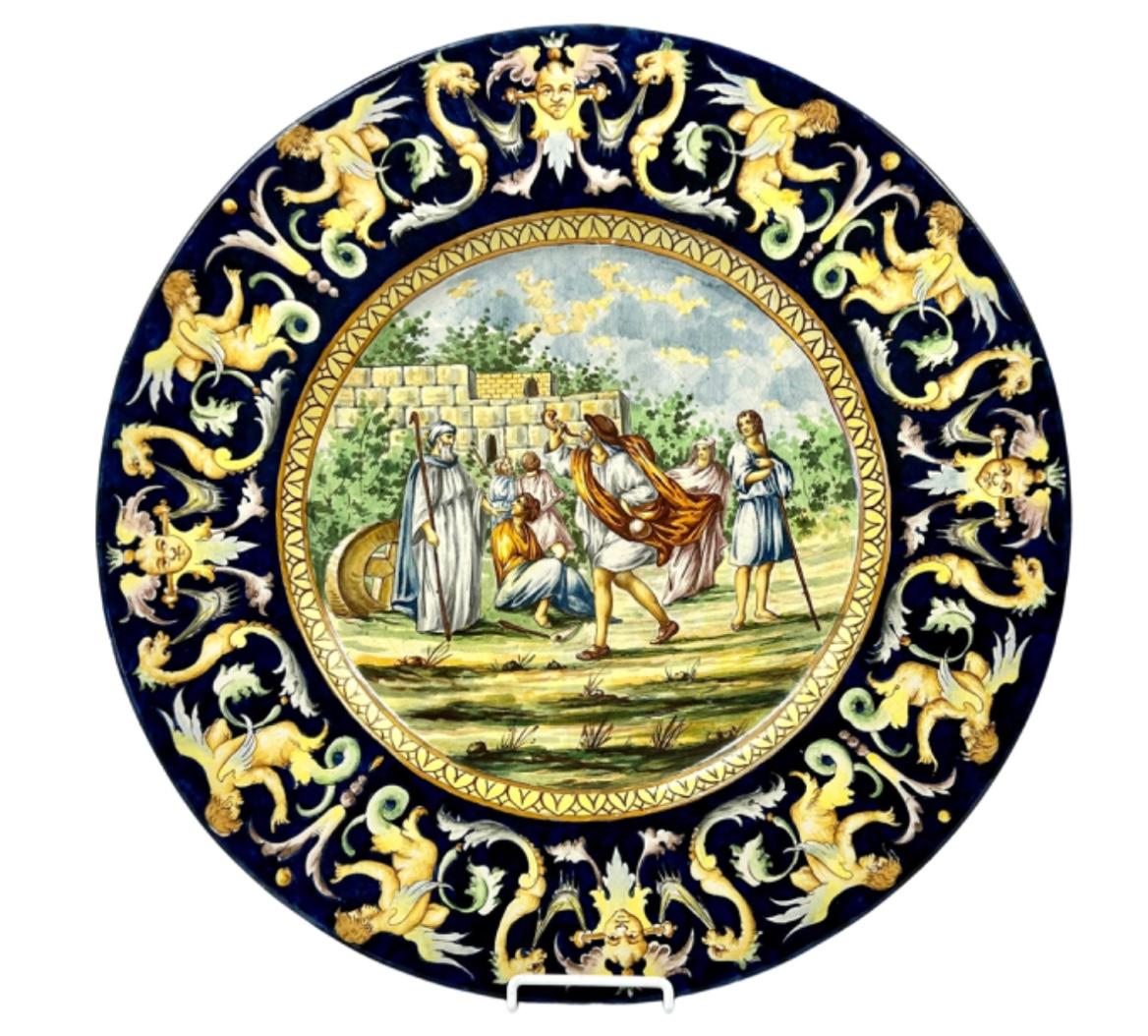 Large 19th century Italian Majolica charger in the Renaissance style. Charger has faces, dragons, and angels on wide cobalt border. Center of charger depicts an Italian village scene in hues of gold, light blue, rust, and green. Marked on reverse