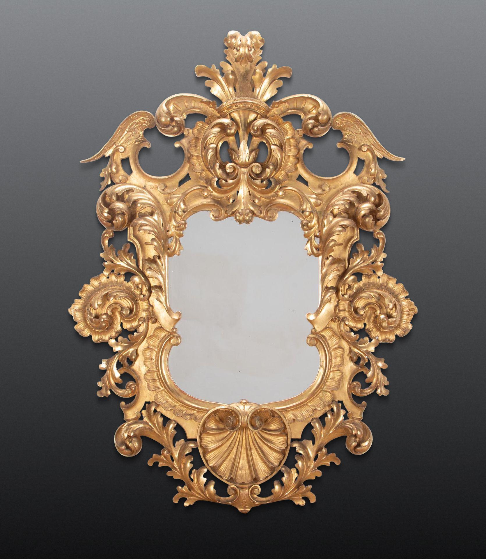 Un audacieux miroir en bois doré de Florentine du début du XIXe siècle, de grande taille et de forme harmonieuse, dans le style du XVIIIe siècle. Avec un cimier à plumets, flanqué d'ailes et de rinceaux élaborés, se terminant par une coquille