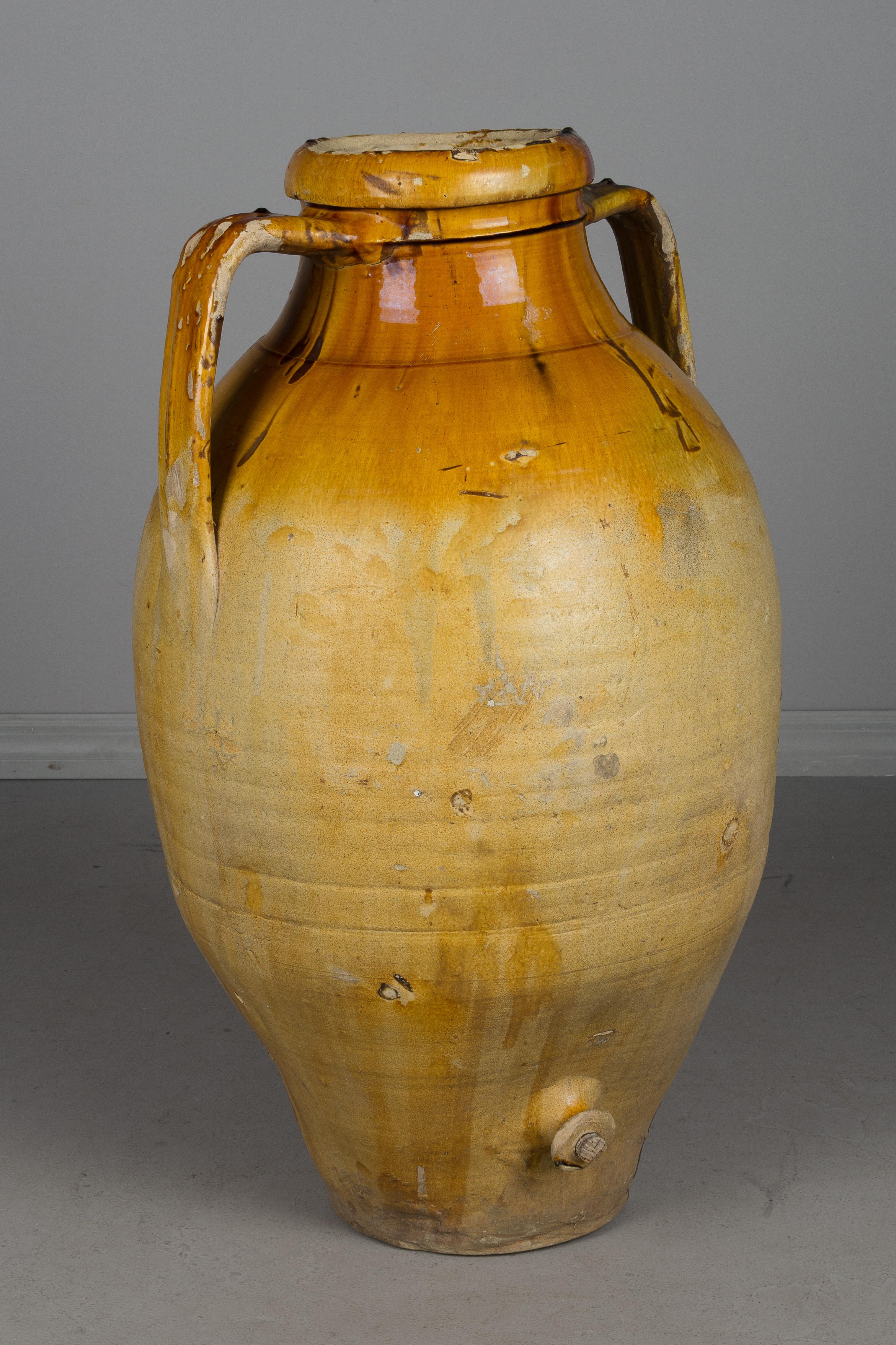 A large 19th century glazed terracotta two-handled pottery urn used for storing olive oil with a small corked spigot at the bottom. Bright yellow ochre glaze at the top. From the Apulia region of Southern Italy. A nice sculptural element for the