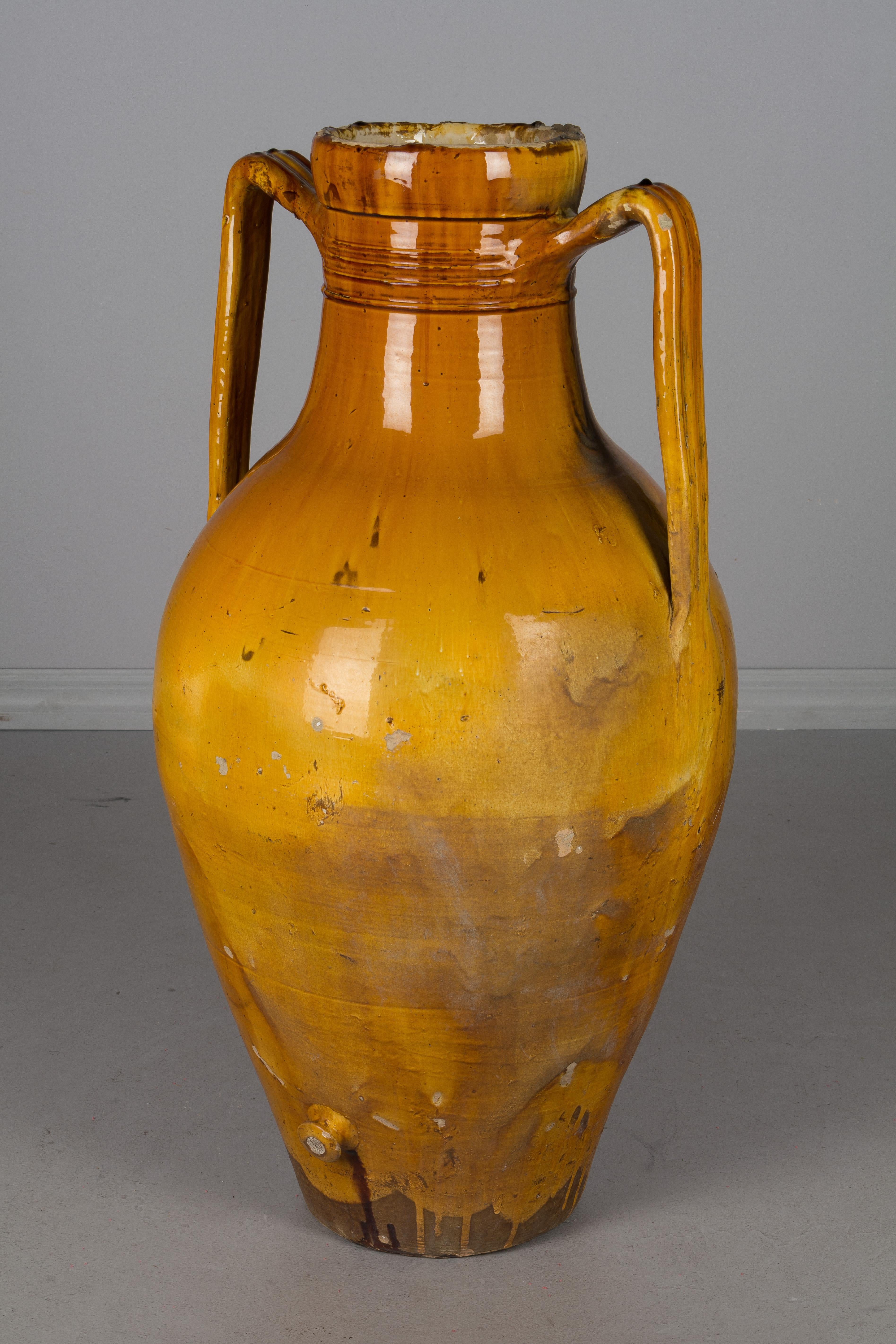 A large 19th century glazed terracotta two-handled pottery urn used for storing olive oil with a small corked spigot at the bottom. Bright yellow ochre glaze. From the Apulia region of Southern Italy. A nice sculptural element for the garden or