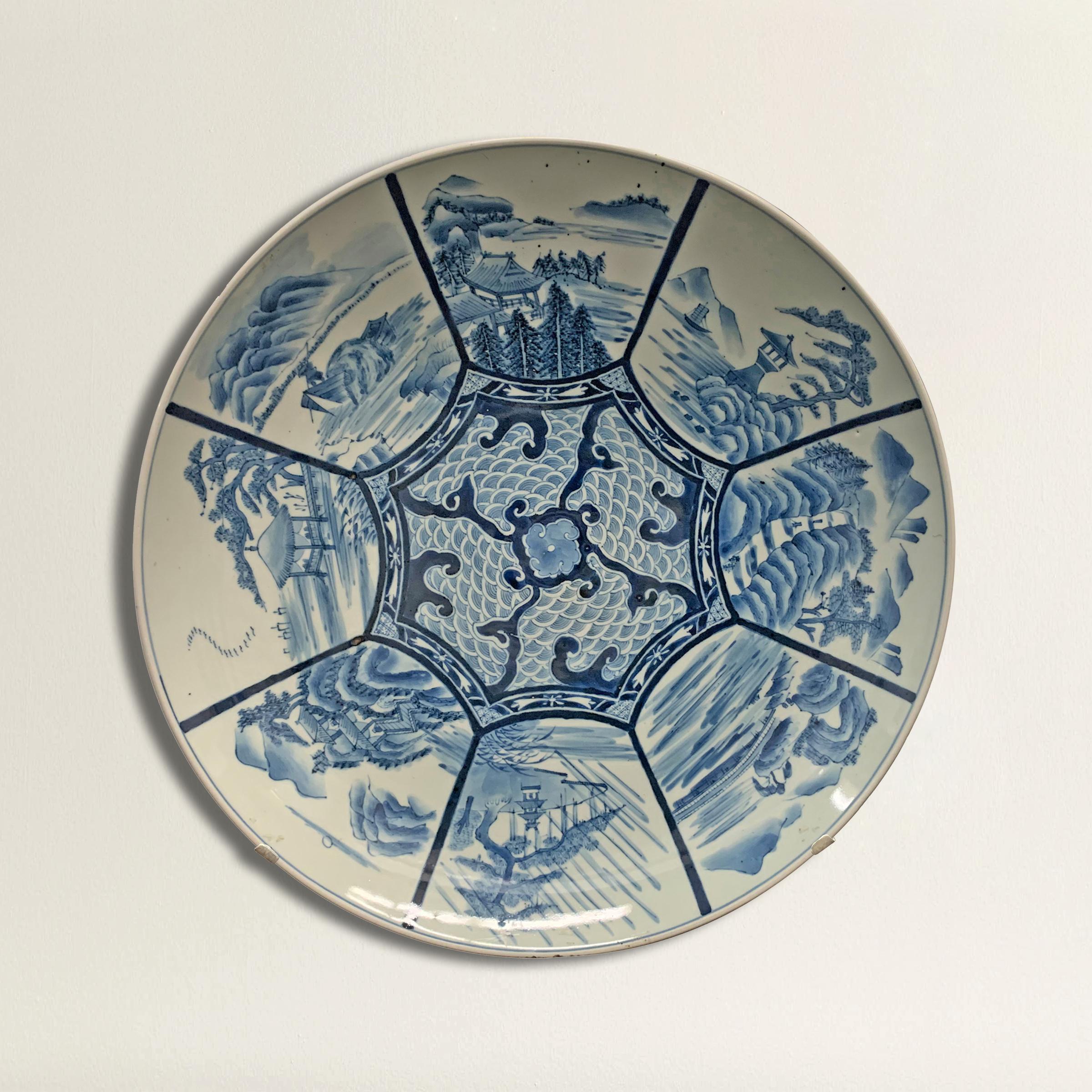 A large 19th century Japanese blue and white platter depicting several pagodas in garden landscapes amidst turbulent clouds and pine trees. Custom steel wall mount included for display purposes.