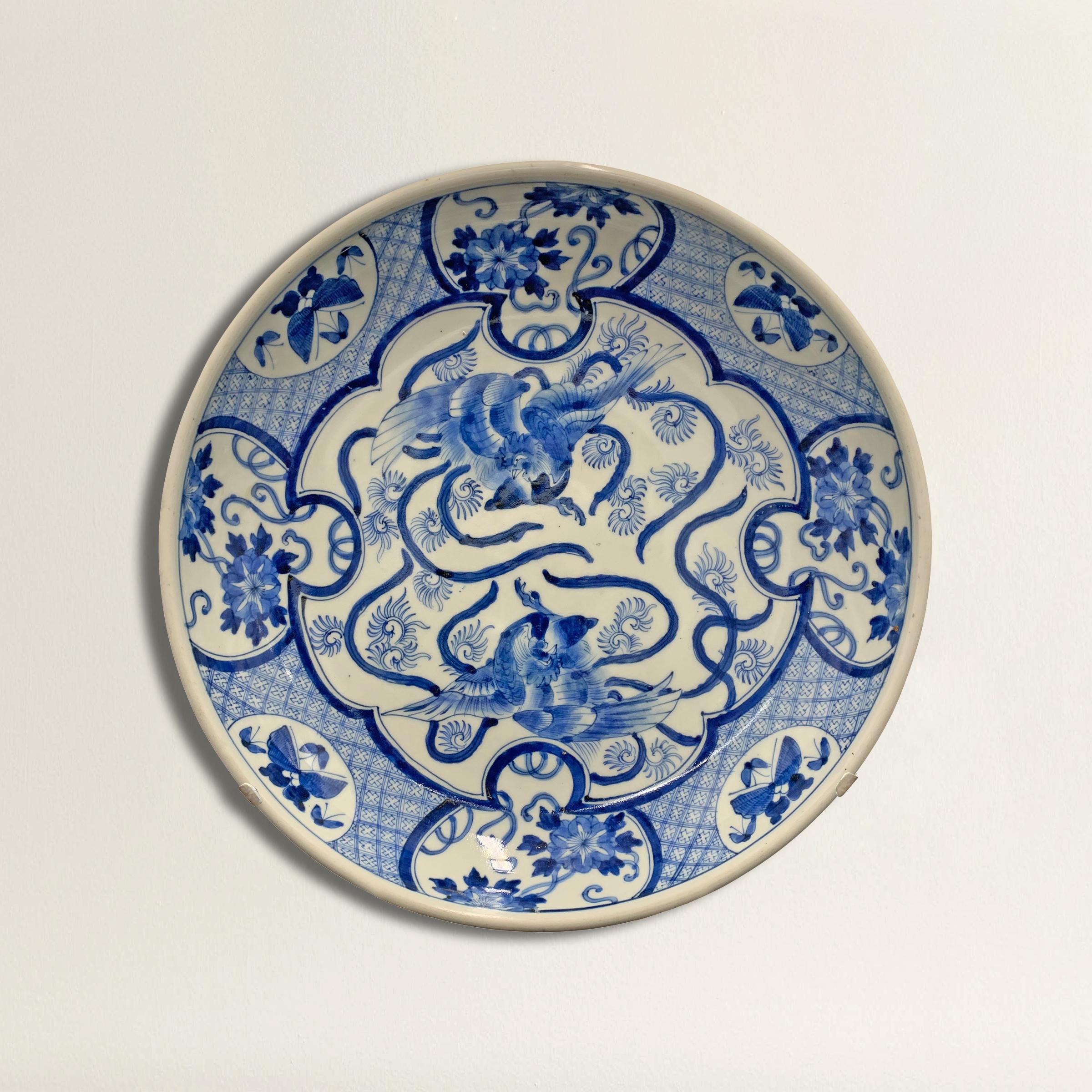 A large 19th century Japanese blue and white platter depicting two Phoenix in flight in the center surrounded by a border of auspicious flowers and a geometric frame. 
 Custom steel wall mount included for display.