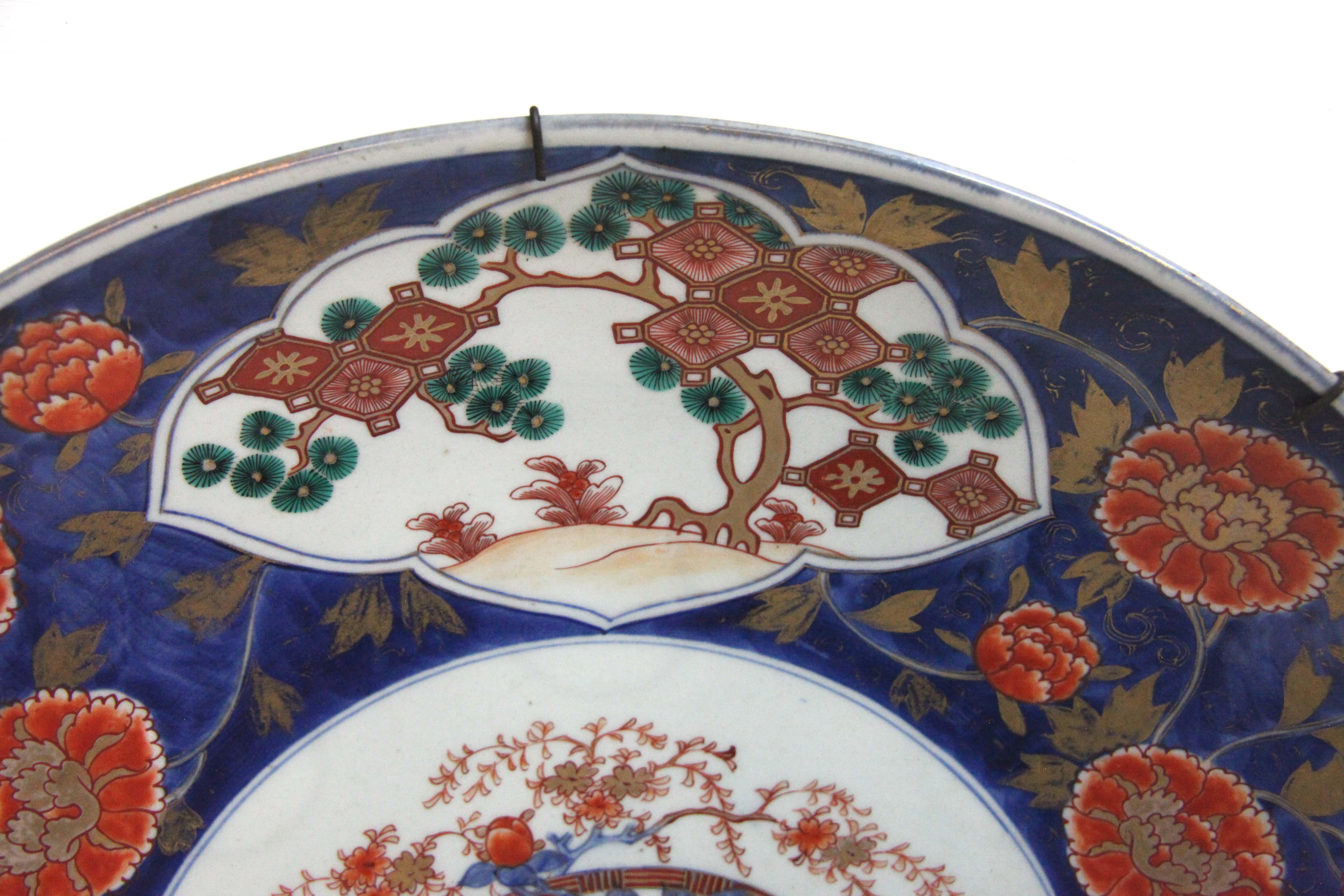 Large 19th century Japanese Imari charger, the central floral basket surrounded by alternating panels of trees and flowers and flowers on a cobalt ground with gilt leaves.