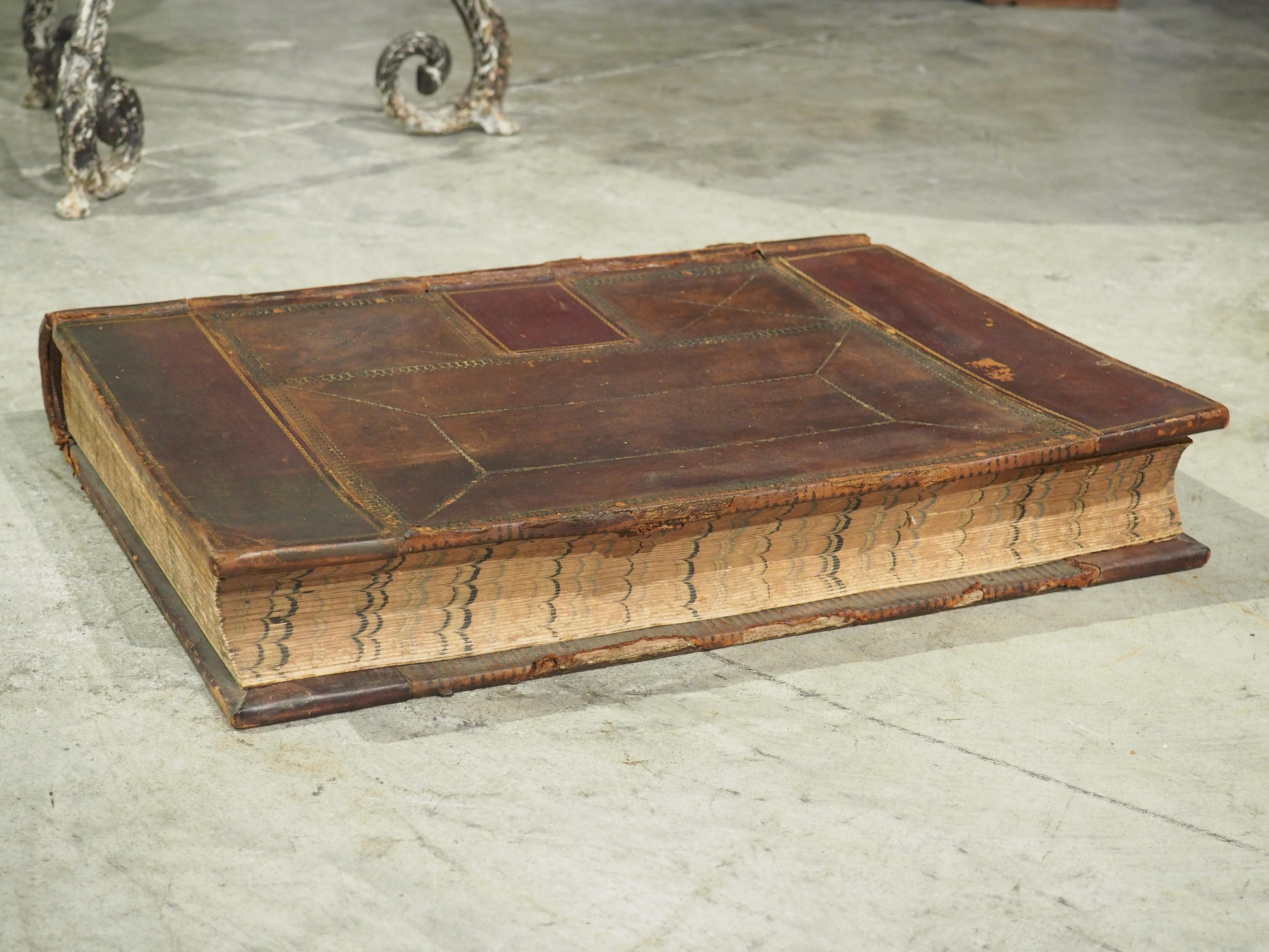 A massive tome, weighing over 20 lbs, this large and decorative leather-bound ledger is from the late 1800’s. Both covers are comprised of sewn leather (utilizing burgundy and dark brown hues), arranged in rectilinear patterns. Prominent ridges can