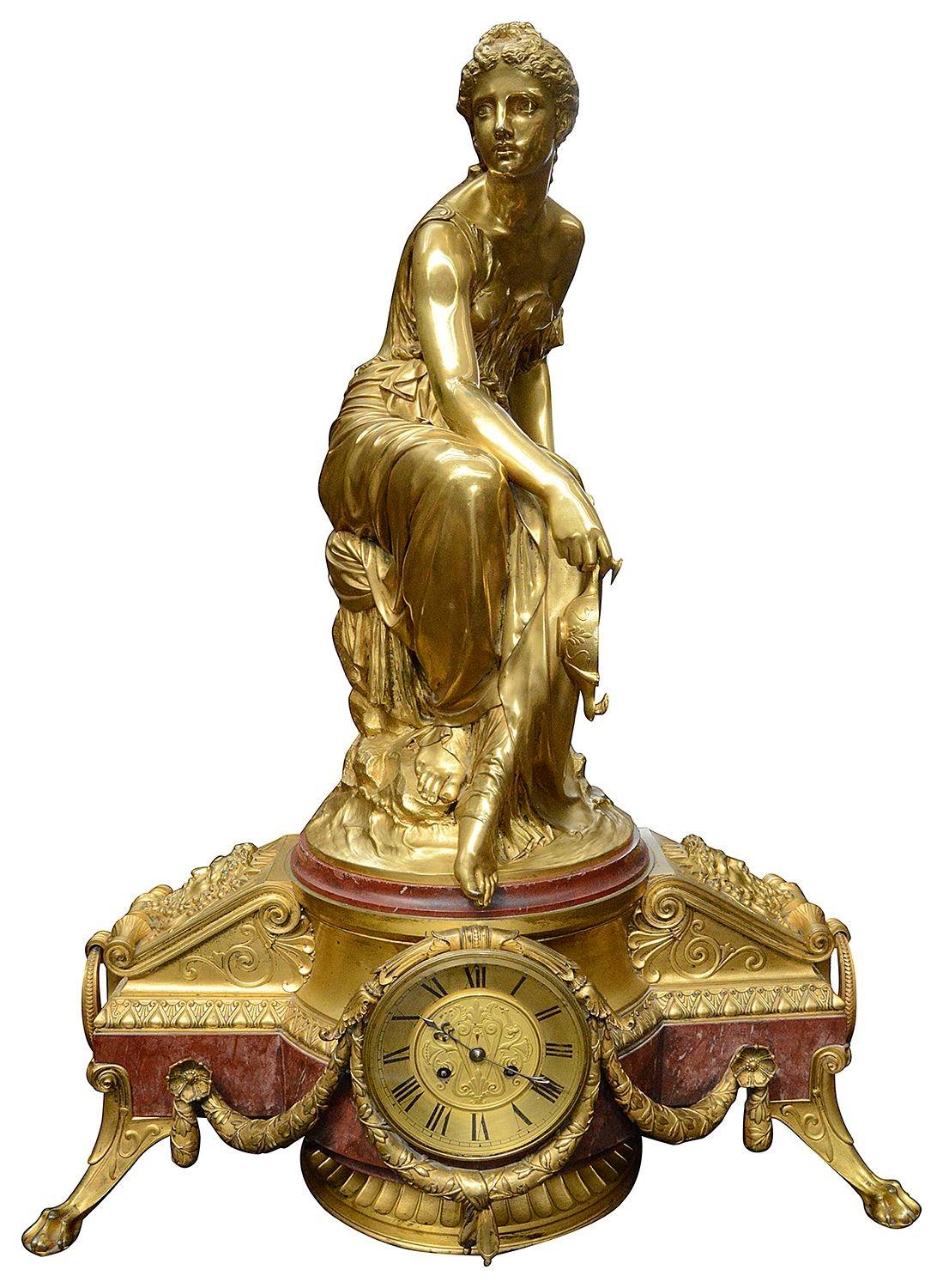 Une spectaculaire horloge française du XIXe siècle en marbre rouge et en bronze doré, avec un beau Madian assis tenant une lampe à huile au-dessus de supports masqués avec des poignées en anneau de chaque côté du cadran de l'horloge. La durée de