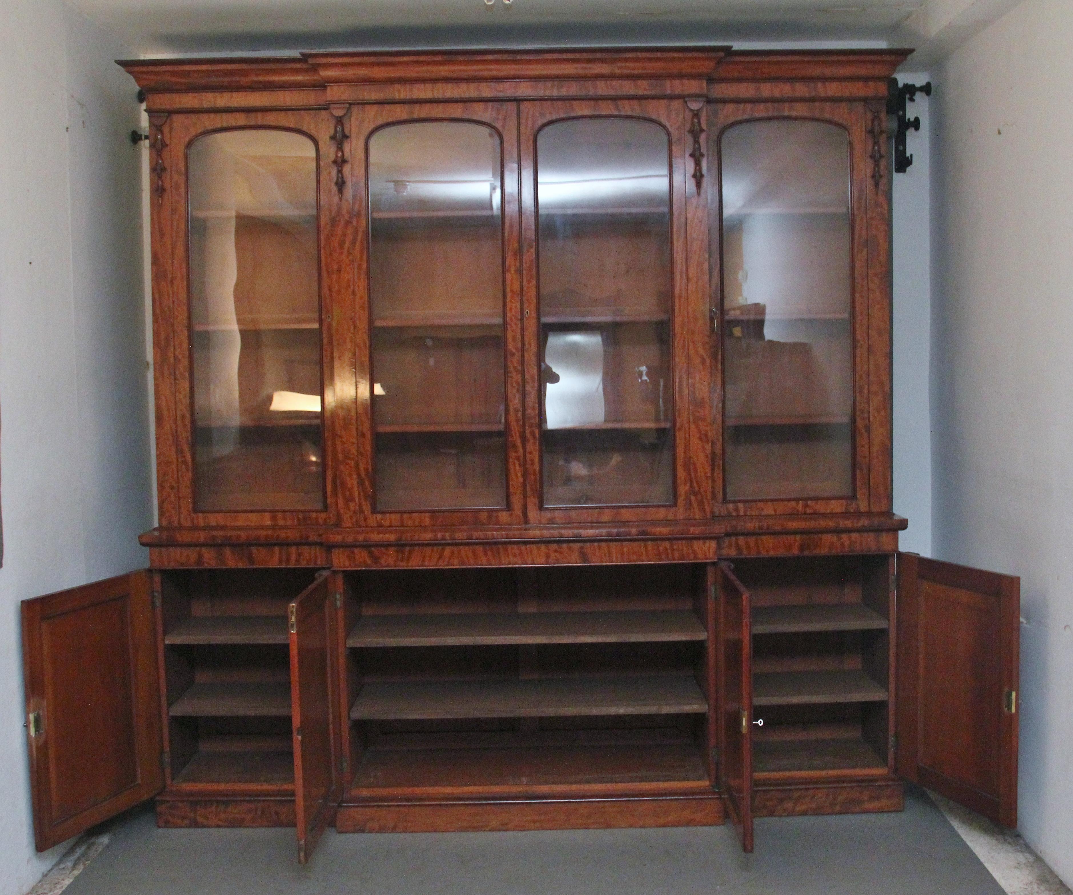A fabulous quality early 19th Century mahogany breakfront bookcase, the stepped moulded cornice above four large moulded and arched glazed doors, with decorative carved moulding to the side of each door, opening to reveal three adjustable shelves