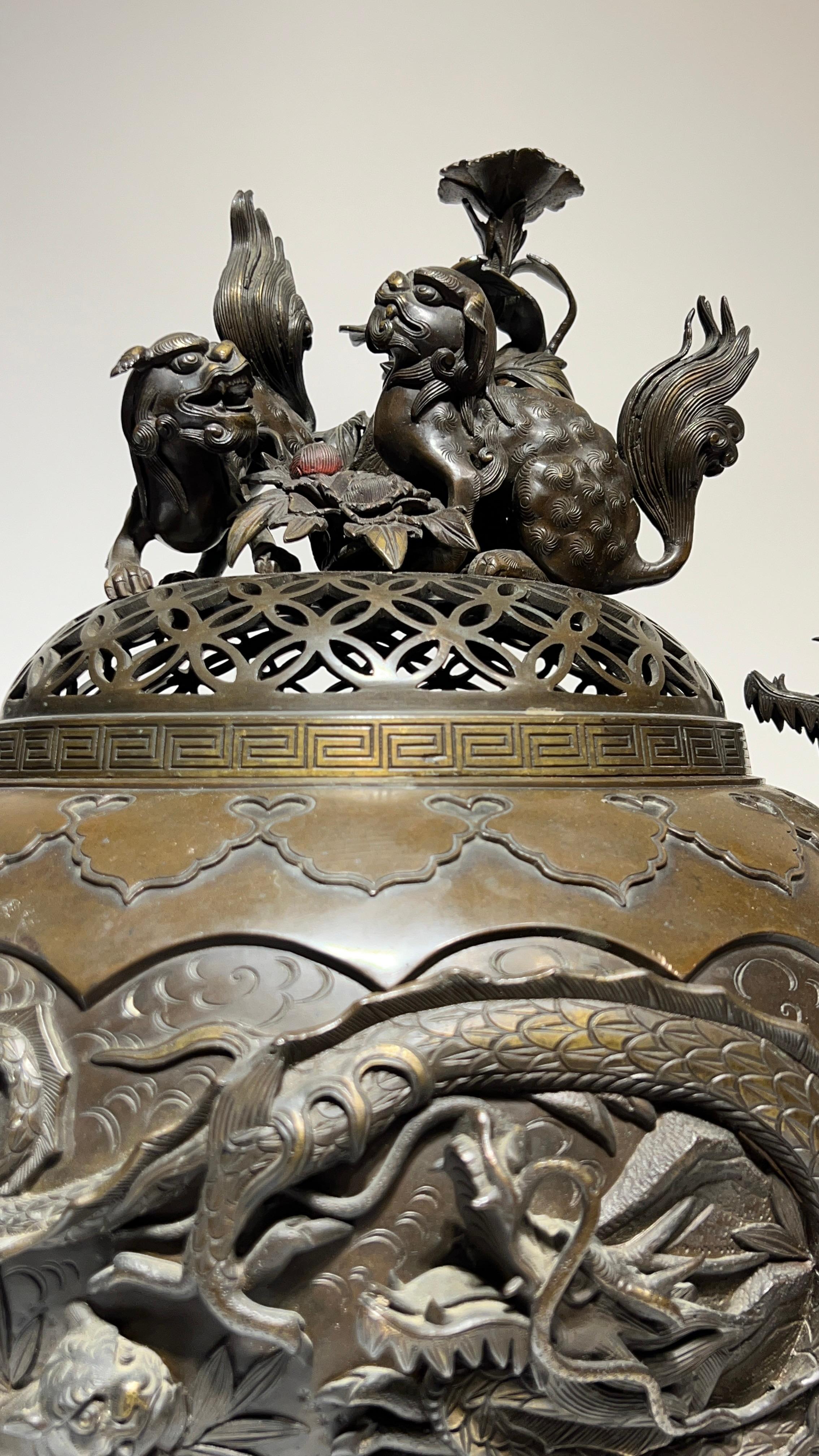 Finely sculpted and cast Meiji period bronze censer with dragon form handles, depicting panther and dragon on one side, and exotic birds on opposite side, cast in three sections and surmounted by a reticulate cover depicting foo lions among