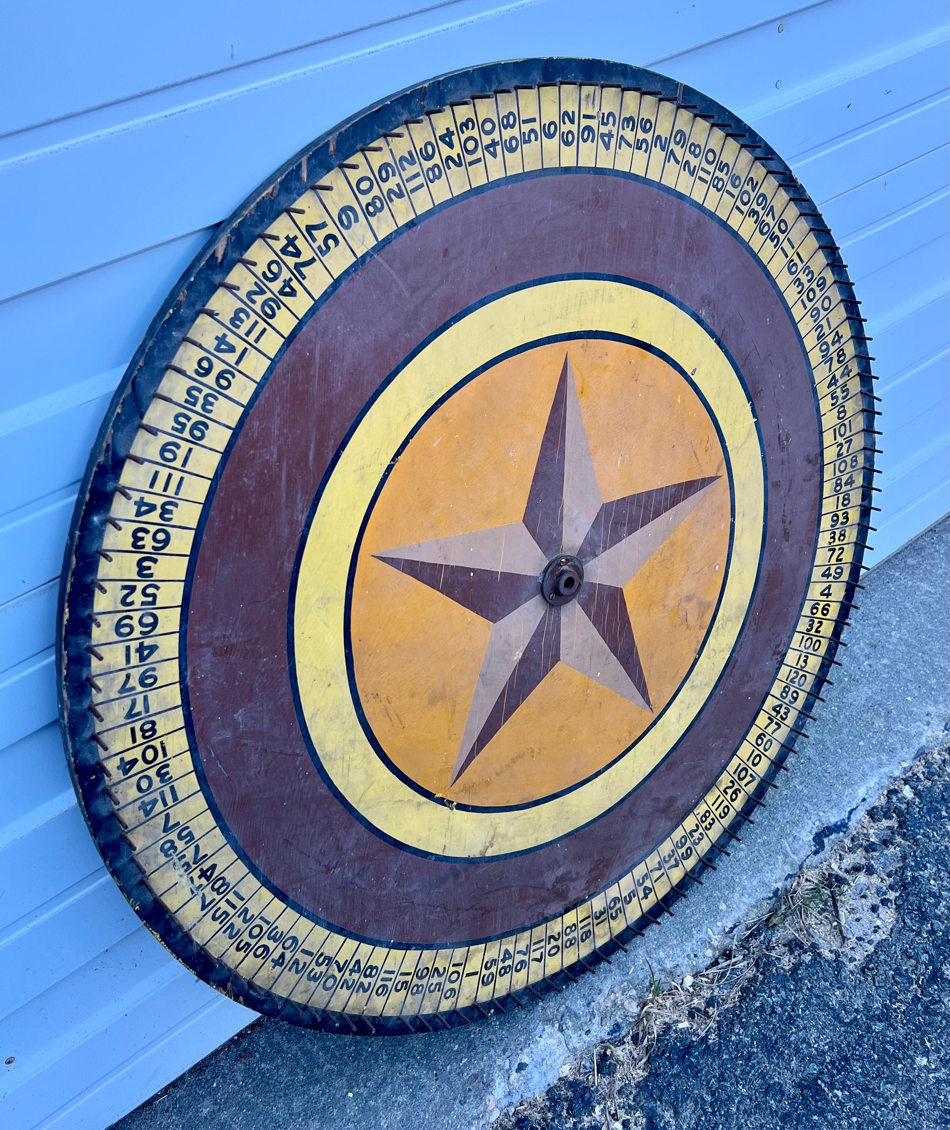 Large 19th century wooden gaming wheel with hand-painted face including numbers and central nautical star design.  In black, maroon, yellow, and orange paints, with metal dowels separating each number.  Fantastic wall hanging.