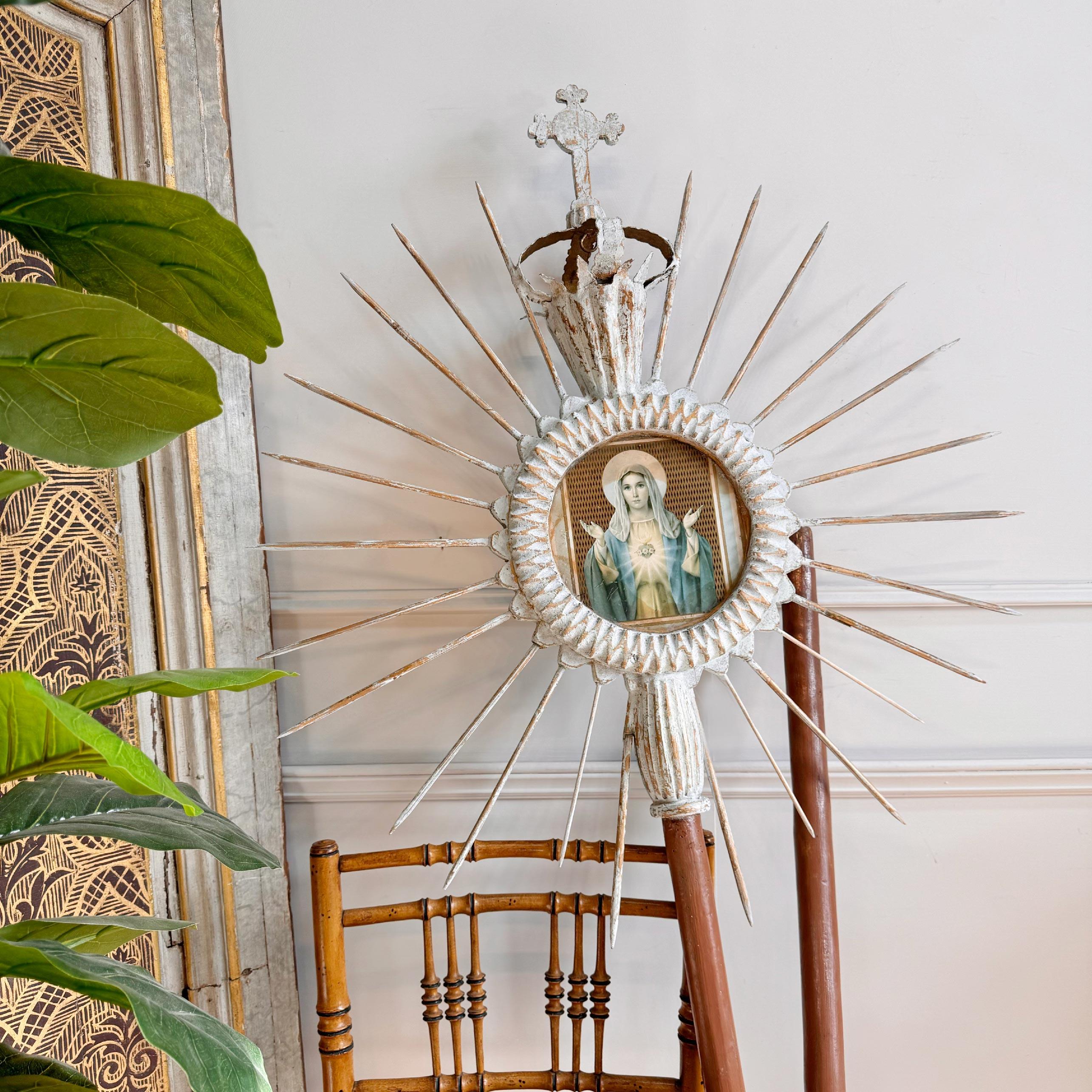 An incredible processional sunburst/cross, wooden rays emanate from the central image of the Virgin Mary set behind glass, topped with a metal crown and cross. The sunburst is set within a pole that would have been carried aloft during religious