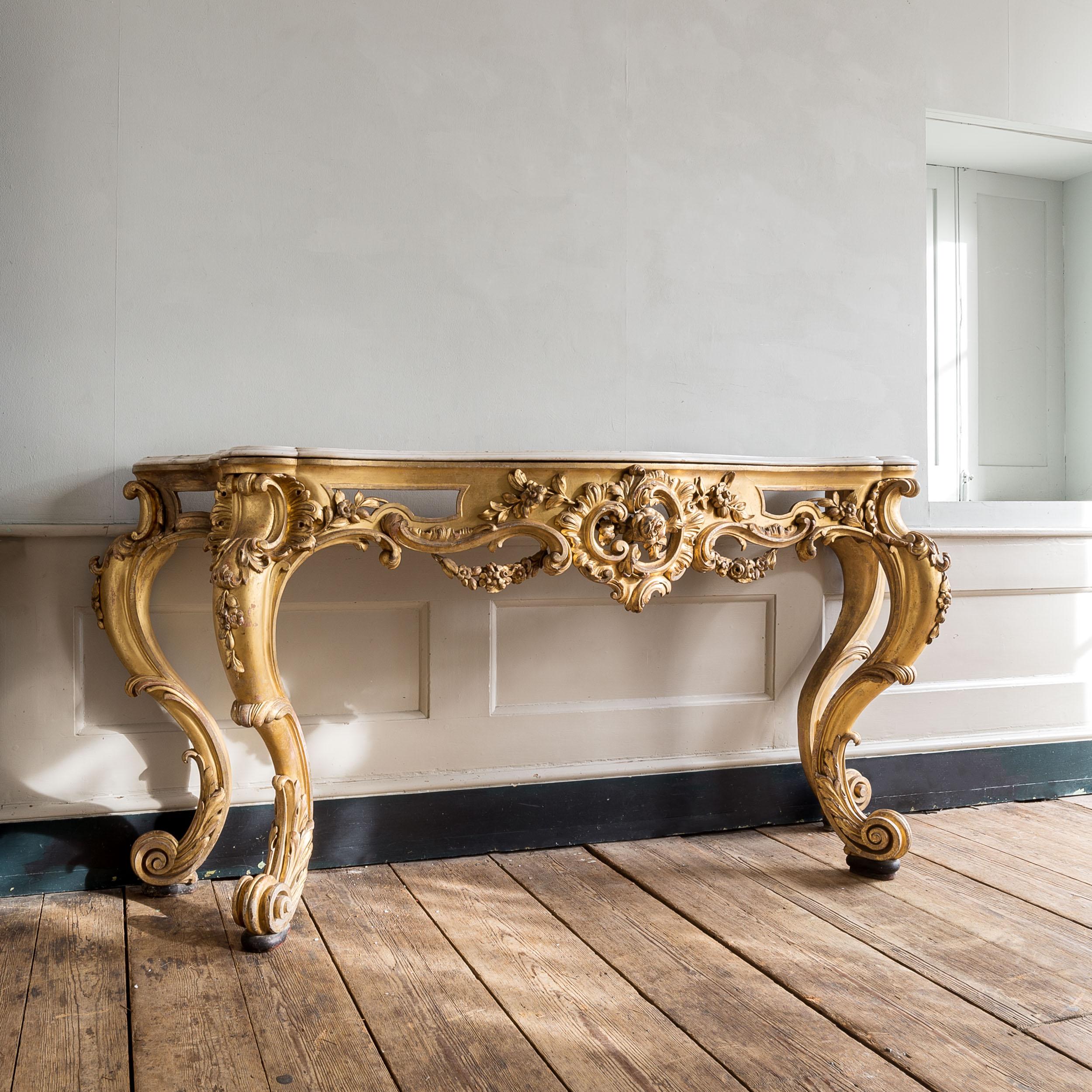 A large nineteenth century English Rococo giltwood console table, with shaped and moulded Carrara marble top, the table boldly carved with c and s scrolls, trails and festoons of foliage and a cabochon to the centre. on scrolled feet. English, early