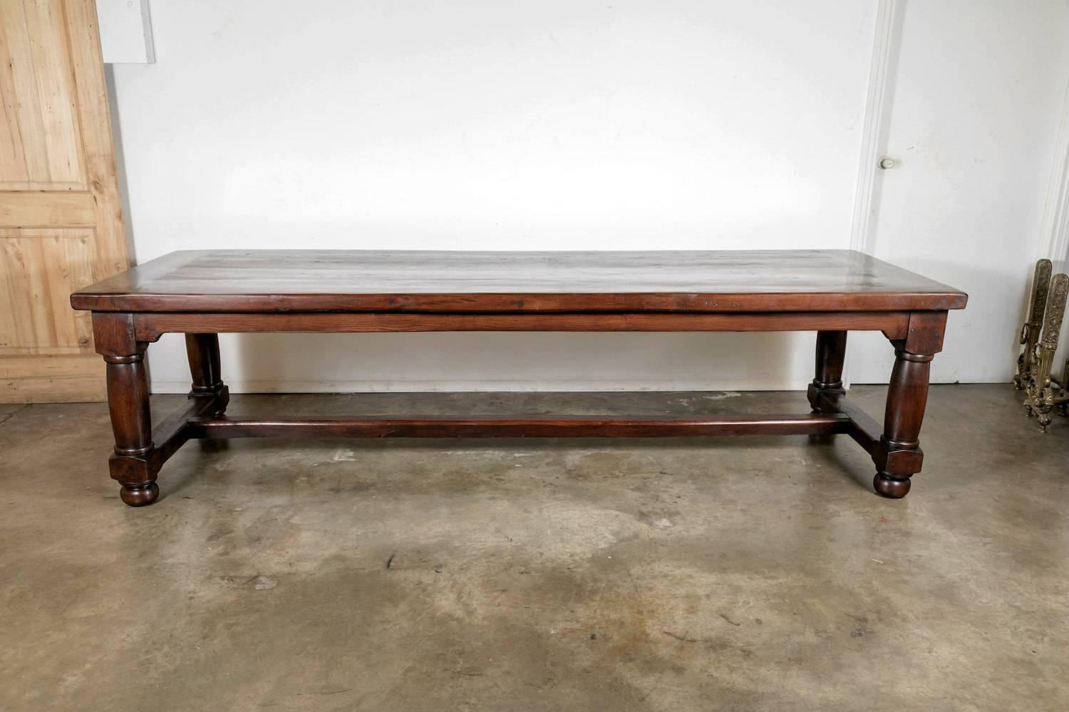 A large rectangular Louis Philippe style farm table, handcrafted in Normandie of solid chestnut with a thick plank top having a cutting/bread board slide on one end and a single drawer on the opposite end. Raised on four baluster legs and joined by