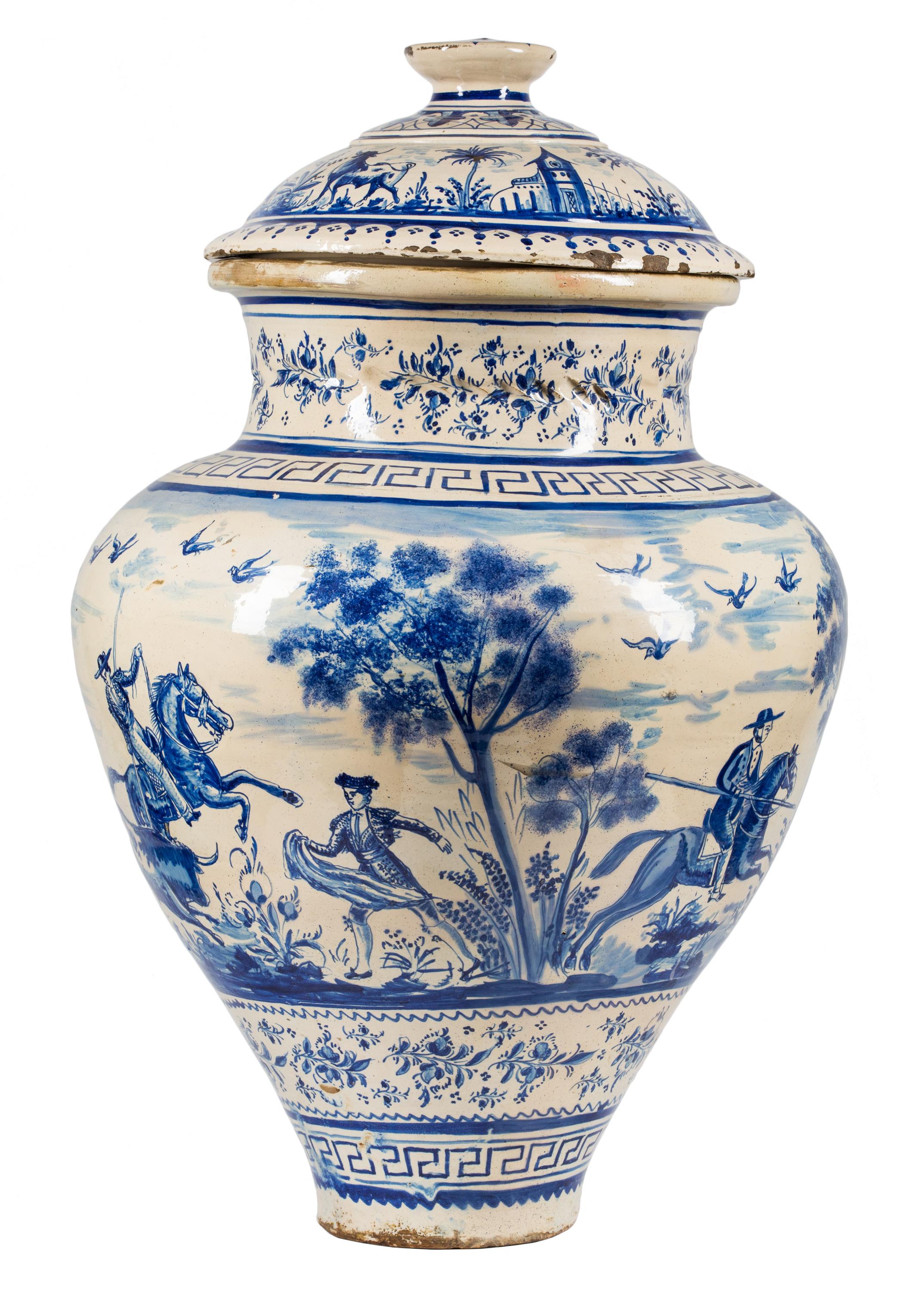 A large (80cm H) 19th century ceramic jar with lid made in the Triana district of Seville, Spain. It is hand painted in cobalt blue glaze over a milk white tin slip in montería (hunting) style, with bulls, mounted picadors and a hunter with rifle in