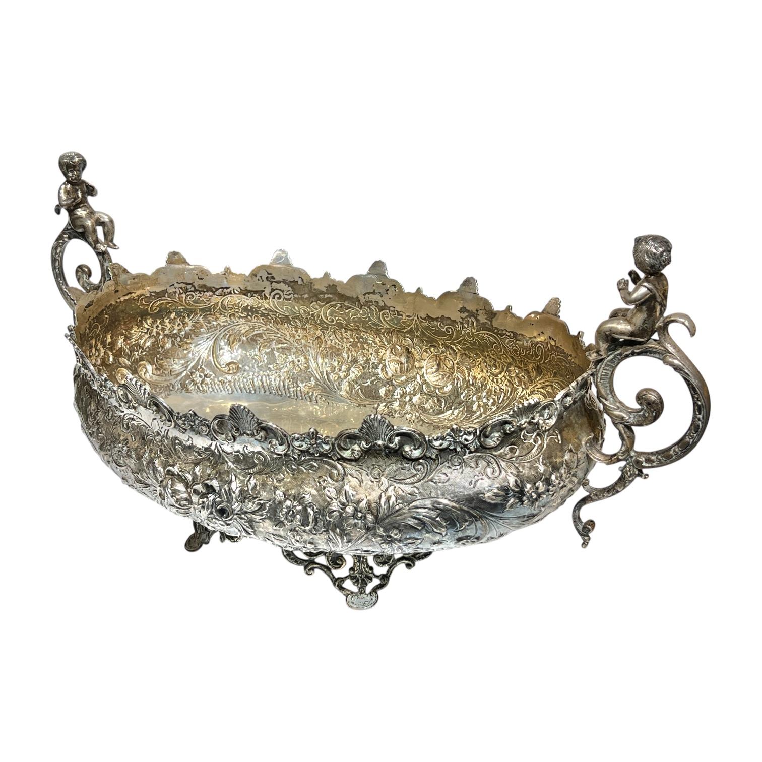Large antique (19th century) European continental sterling silver centerpiece in the neoclassical style, distinguished by its size, 22 by 11 by 11 inches, cherub handles and extensive repousse and chased designs including rocaille, c-scrolls,