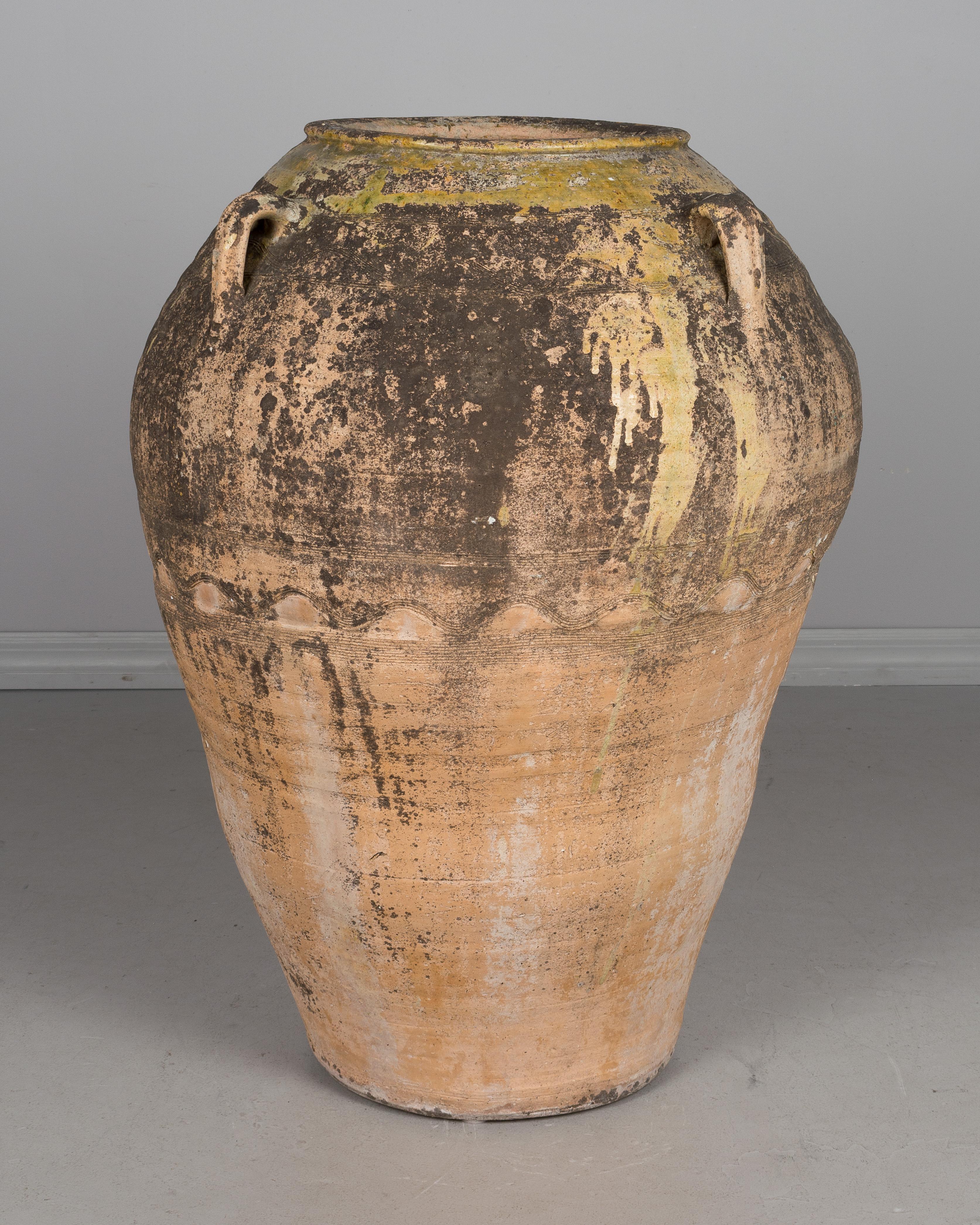 A large Grecian terracotta urn used for storing olives, from the island of Crete. Hand formed with four handles and decorative bands of incised lines. Old mossy patina with remnants of greenish yellow glaze at the top. A nice sculptural element for