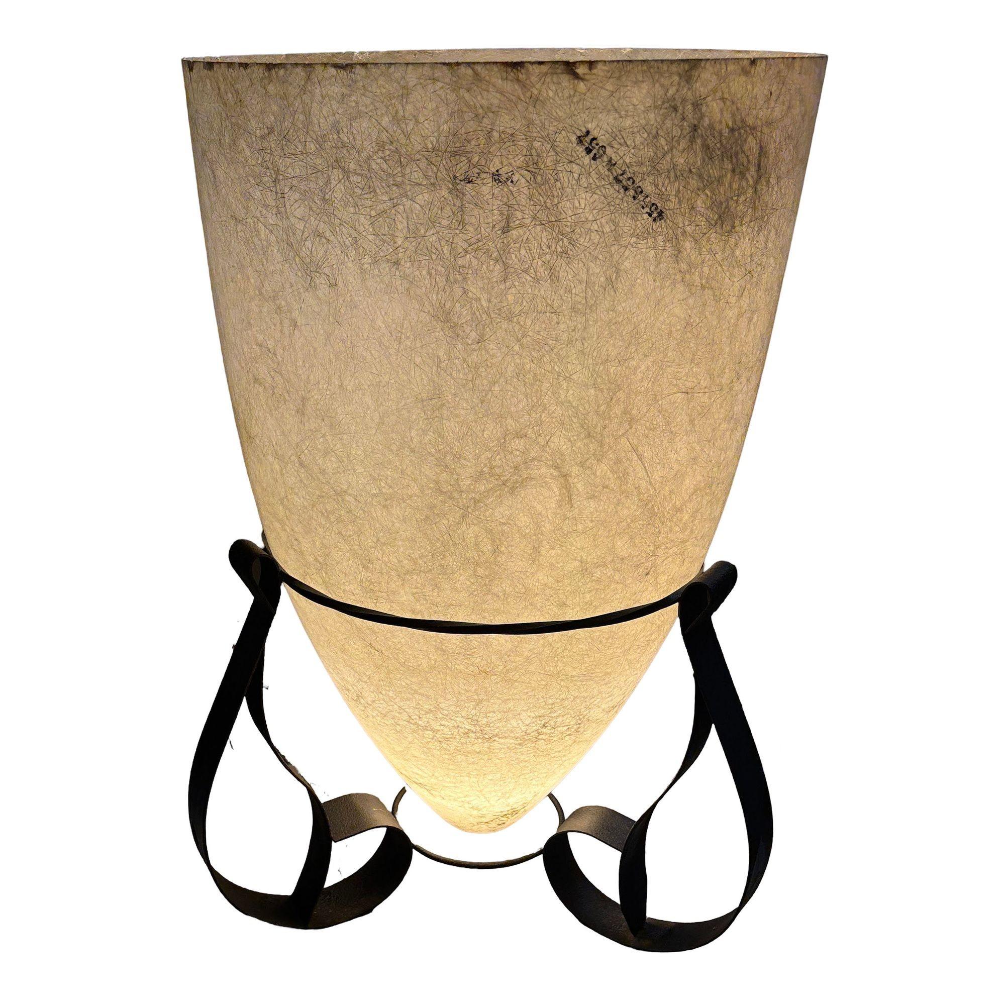 This mid-century modern lamp exudes a timeless charm, featuring a graceful fiberglass cone shade and a sturdy iron base. The shade's soft, creamy white hue complements the dark, antique bronze finish of the base, creating a striking visual contrast.