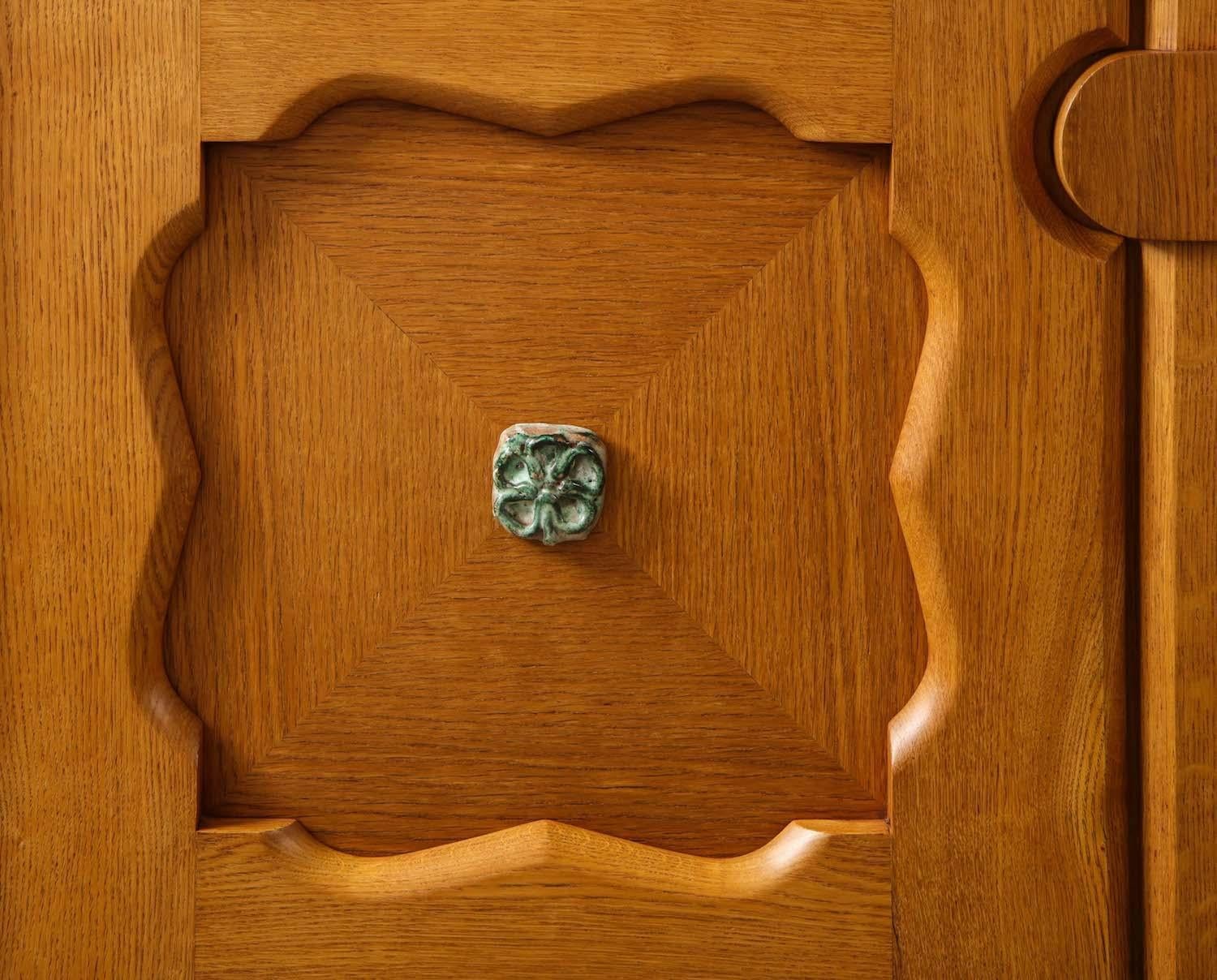 Oak, glazed earthenware, brass. Large scale cabinet of waxed oak with interior shelves and ceramic appliques to door fronts. Wood has been refinished.