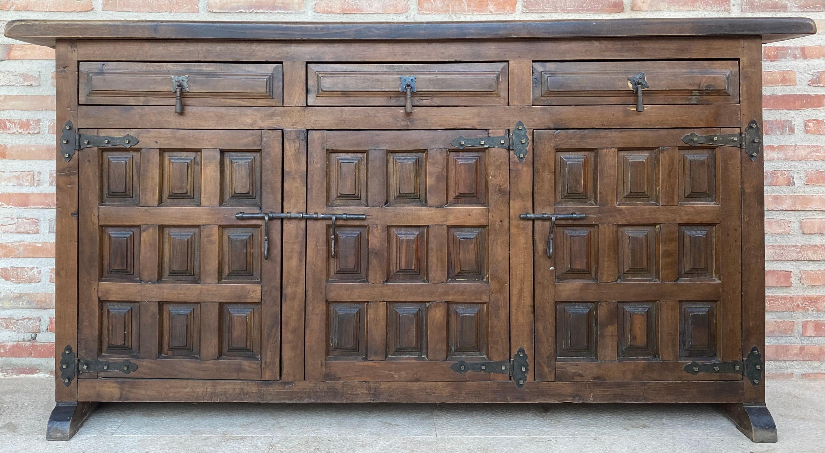 Coming from northern Spain, constructed of solid walnut, the rectangular top with molded edge above a shaped box housing three drawers over three doors, the doors faced with solid walnut and raised on a plinth base. The drawers and doors are hand