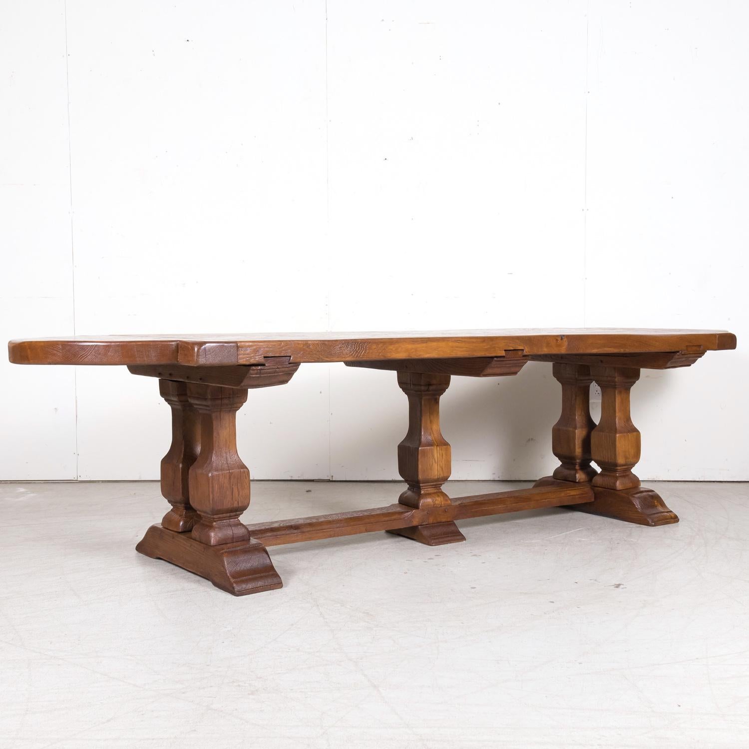 A large 20th century French monastery trestle table handcrafted in Brittany of solid oak having a thick parquet top with rounded ends, circa 1930s. Raised on carved baluster supports resting on plinth bases and joined by a center stretcher with a