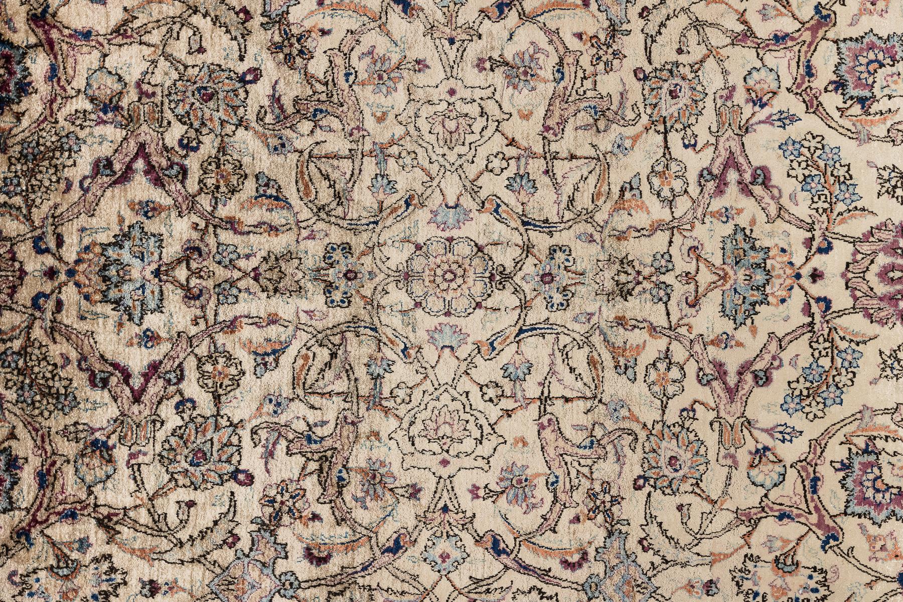 Ce tapis en soie finement tissé de Kashan présente un élégant jeu d'ivoire, de bleus doux, de tons rosés et d'accents plus profonds, disposés dans une composition florale richement étagée. Son motif complexe se déploie comme un jardin continu, avec