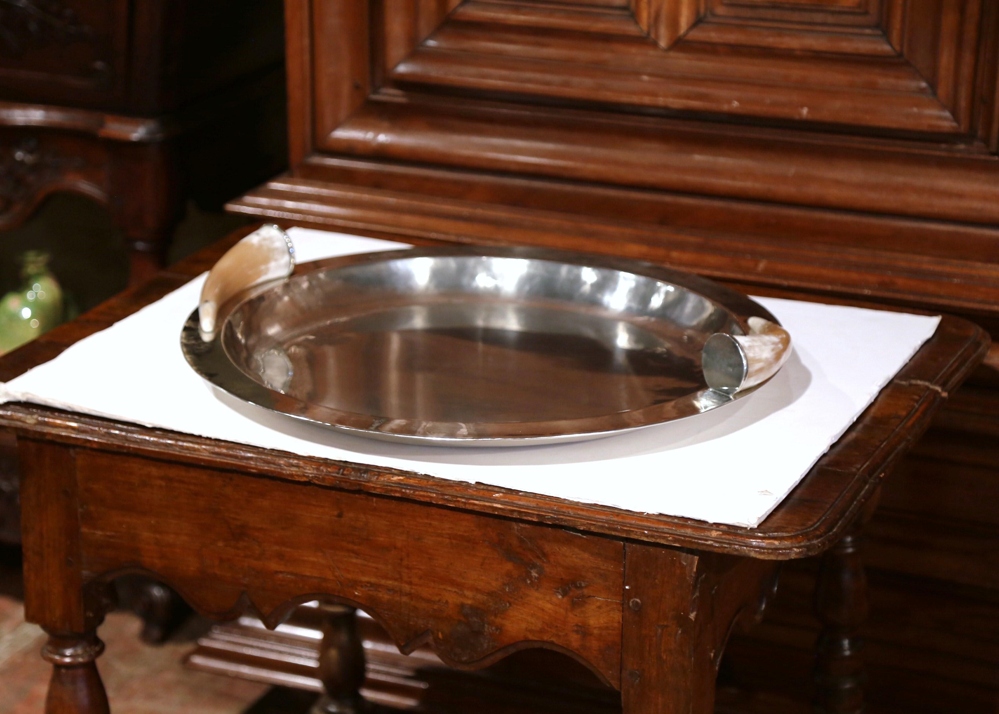 This large serving dish was created in Argentina, circa 1980. Round in shape, the traditional silver plated bowl features a pair of cow horn handles on either side for countryside flair. This unique, rustic platter is in excellent condition with a