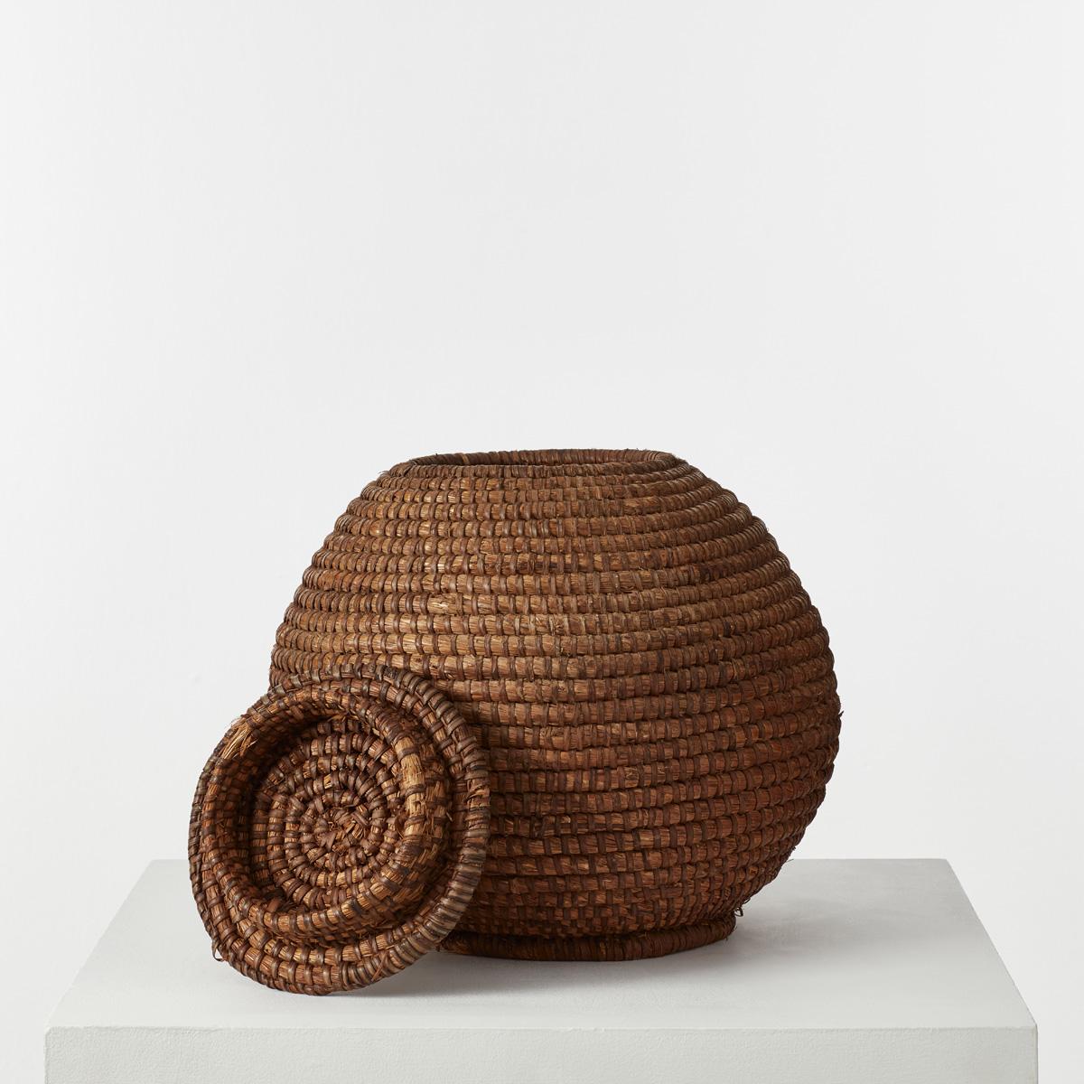 A well-constructed, rounded rattan basket with a lid. It has a characterful rustic caramel colour and would be ideal in a decorative guise or as a useful piece of household storage, for example a laundry basket or waste paper bin.