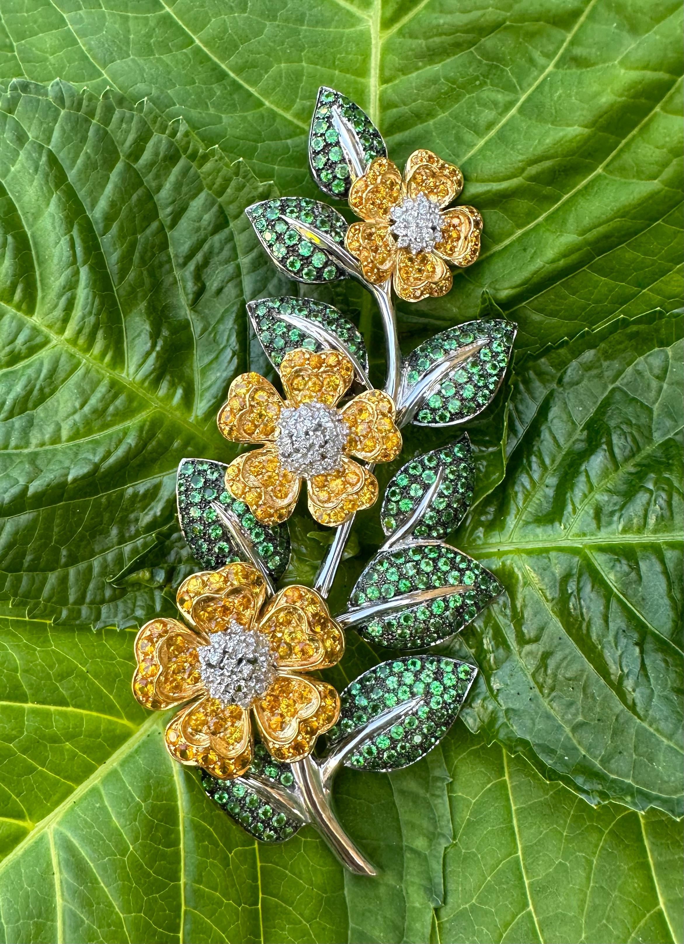 A resplendent, large and stately, 18 karat white and yellow gold three dimensional vining flowers motif estate brooch is comprised of vivid golden yellow sapphires, sparkling white diamonds and green tsavorites, having a combined total estimated