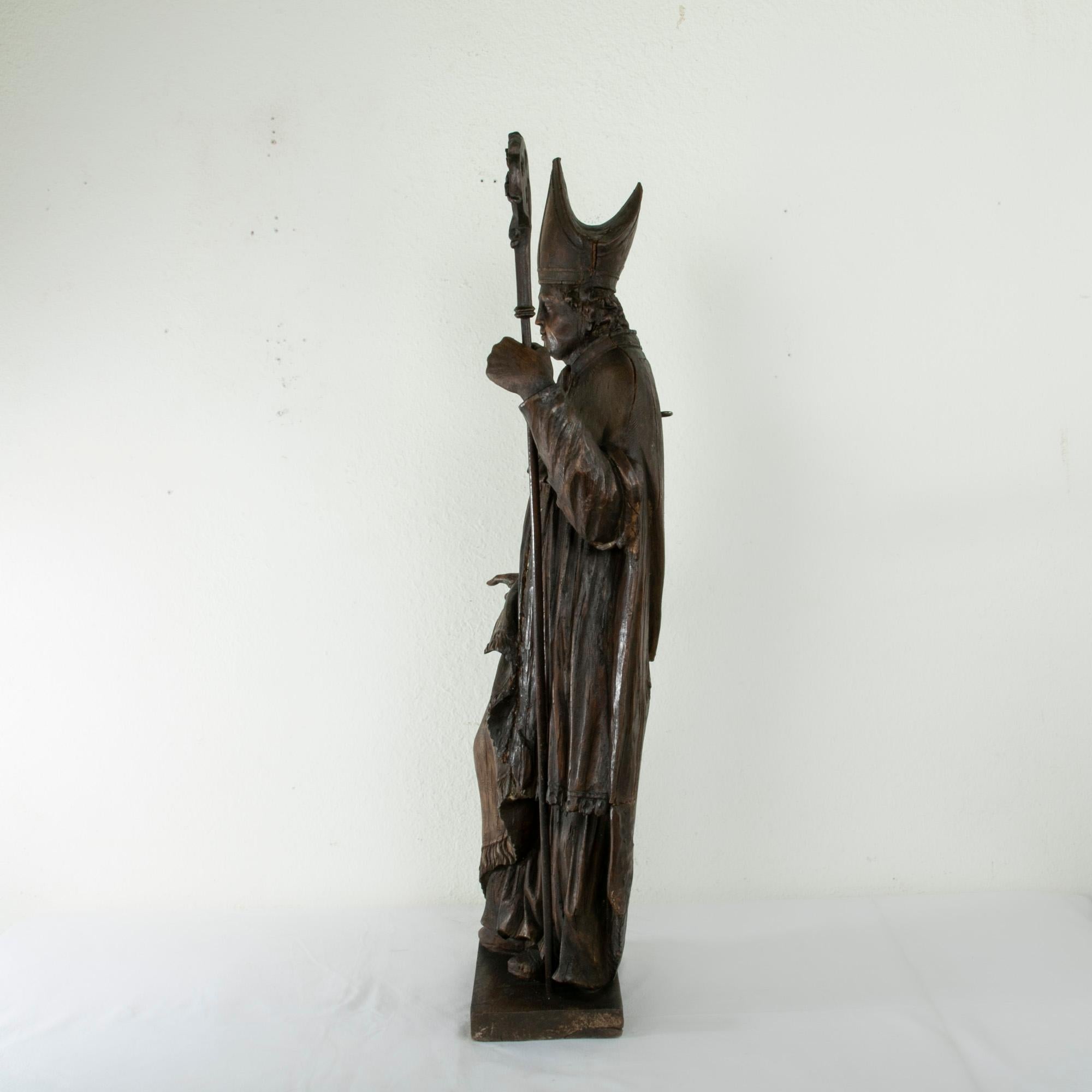 Standing at an impressive 39 inches in height this late eighteenth century French hand carved statue depicts a bishop dressed in his ecclesiastical vestments. A miter crowns his head and a chasuble or cape hangs from his shoulders and wraps around
