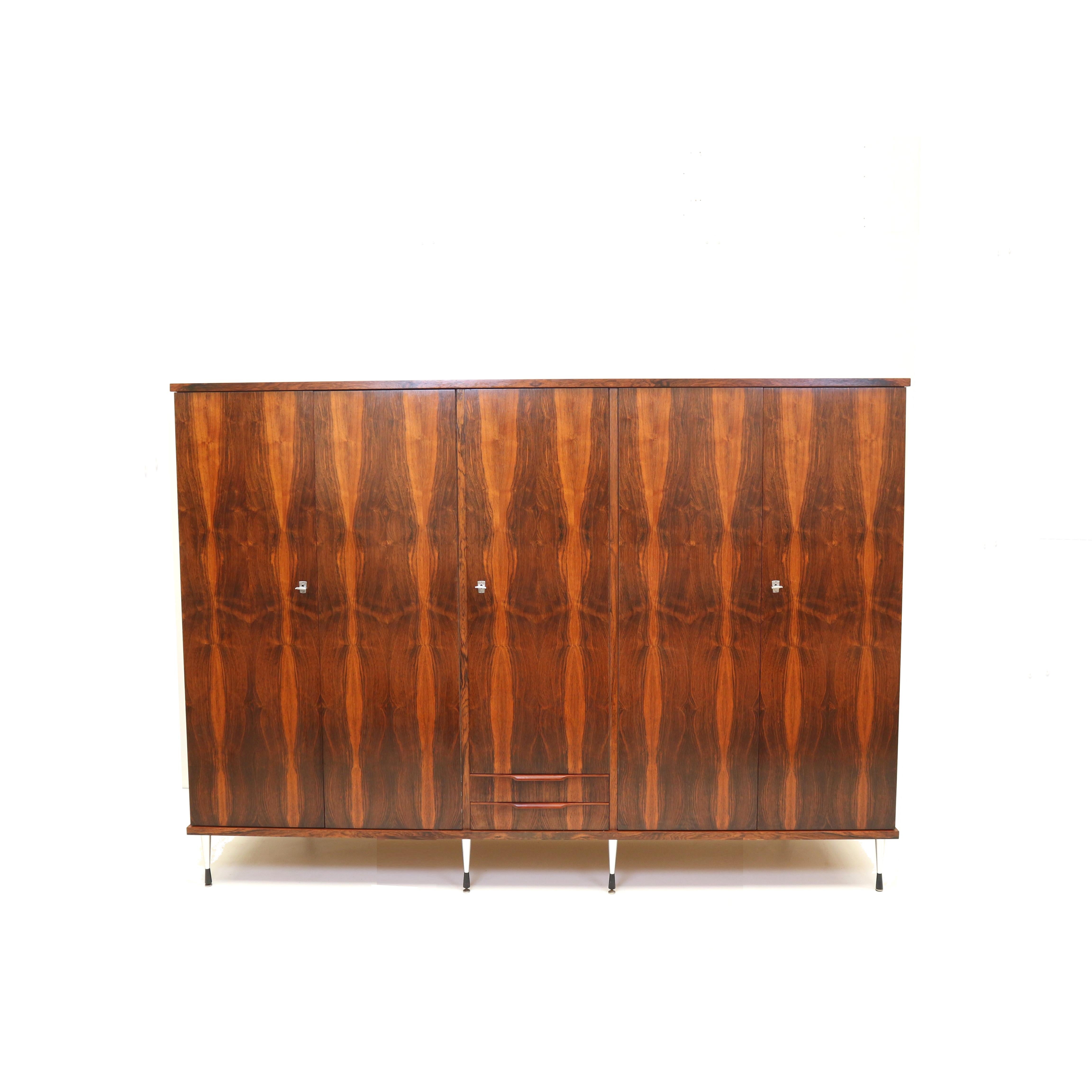 Large 5-door vintage wardrobe in rosewood with stylish adjustable legs in Italian style from the 60s. The wardrobe has two drawers, 4 shelves, 2 hanging rods and a mirror. The wardrobe is in very good condition and has light signs of wear consistent
