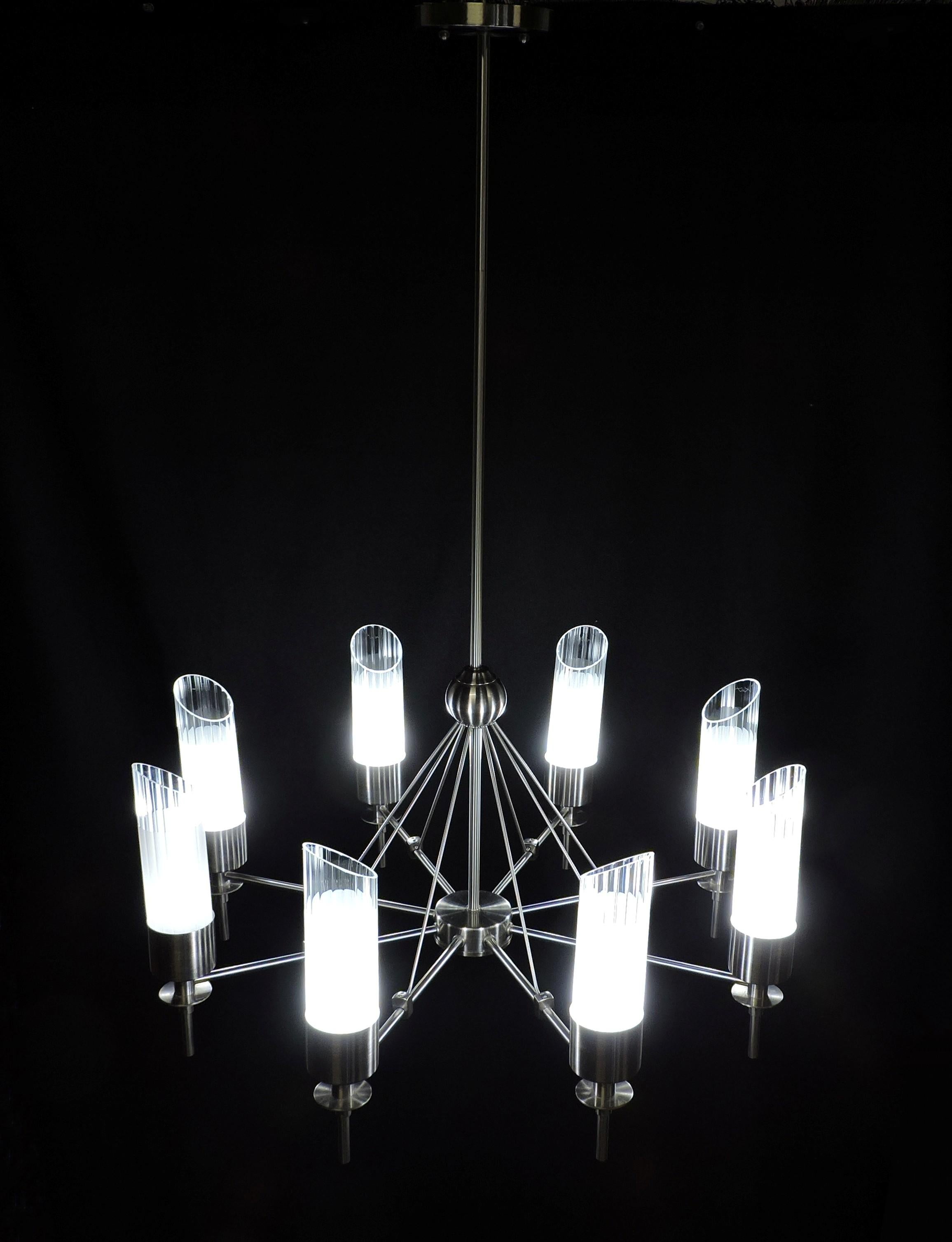 Handsome chandelier by high end design retailer, Luminaire. This impressive 8 light fixture has a stainless steel finish with cylindrical fluted clear glass shades that are partially frosted. It takes eight G9 base bulbs, which can be either halogen