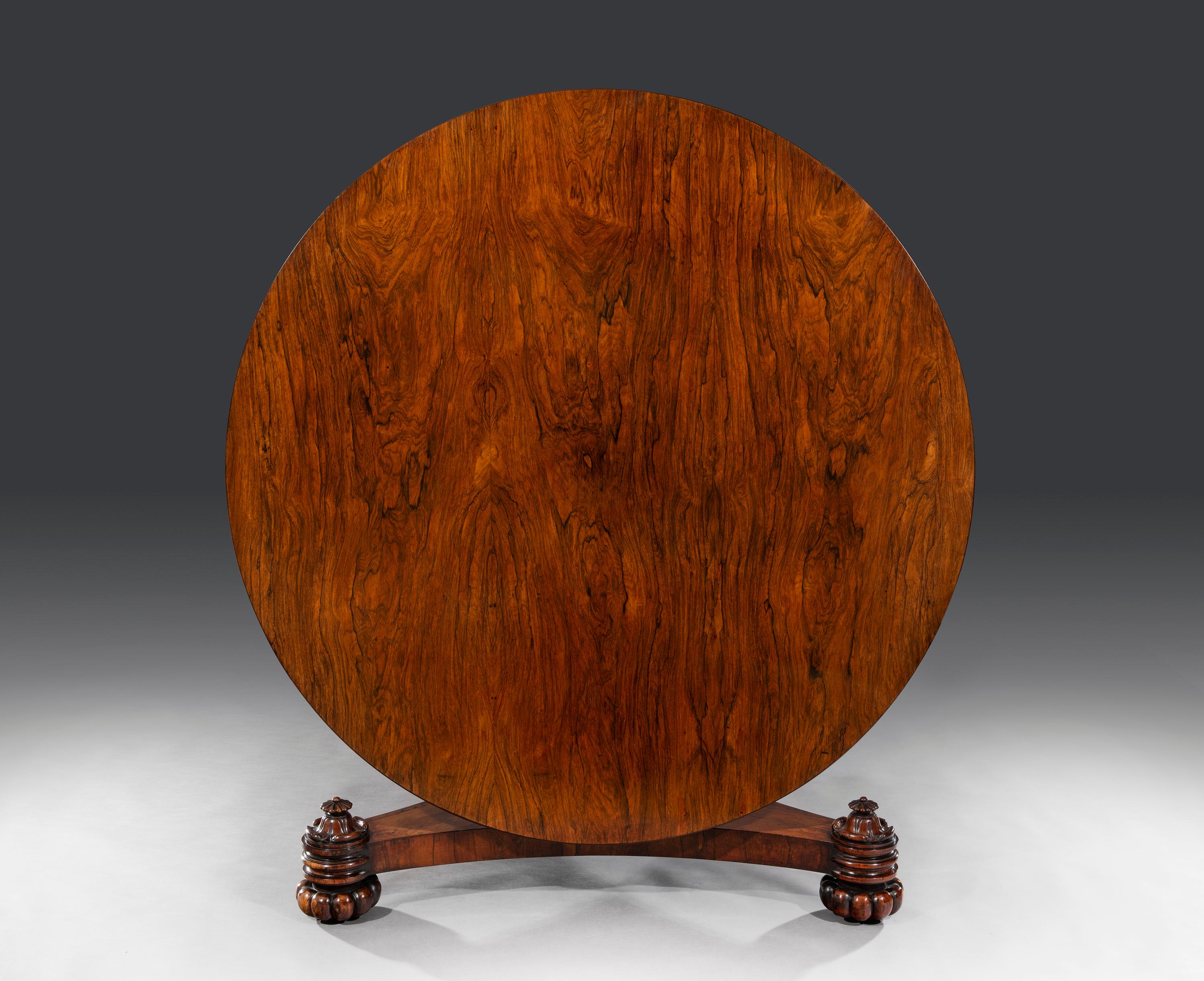 The padouk veneered tilt-top table is 5’ in size. The frieze is cross-banded in rosewood and the carcass is mahogany. The tale top sits on a pedestal and a concave triform base. The table will accommodate up to eight people and stands on a crisply