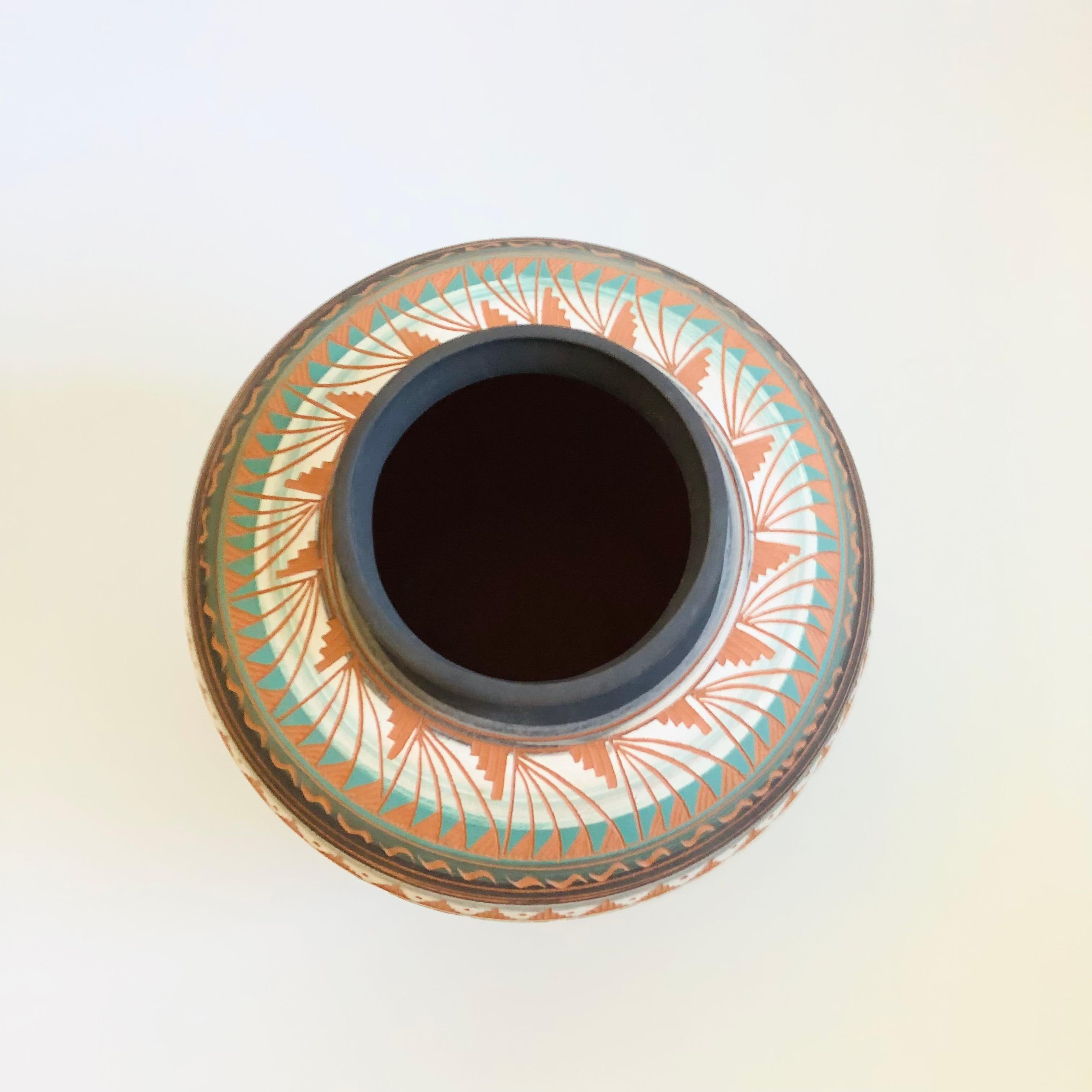 A beautiful vintage hand carved Navajo pottery vase. Bands of color wrap around the sides with a highly detailed pattern that has been hand carved into the sides of the vase exposing the natural terra cotta color of the clay below. Nice large size.