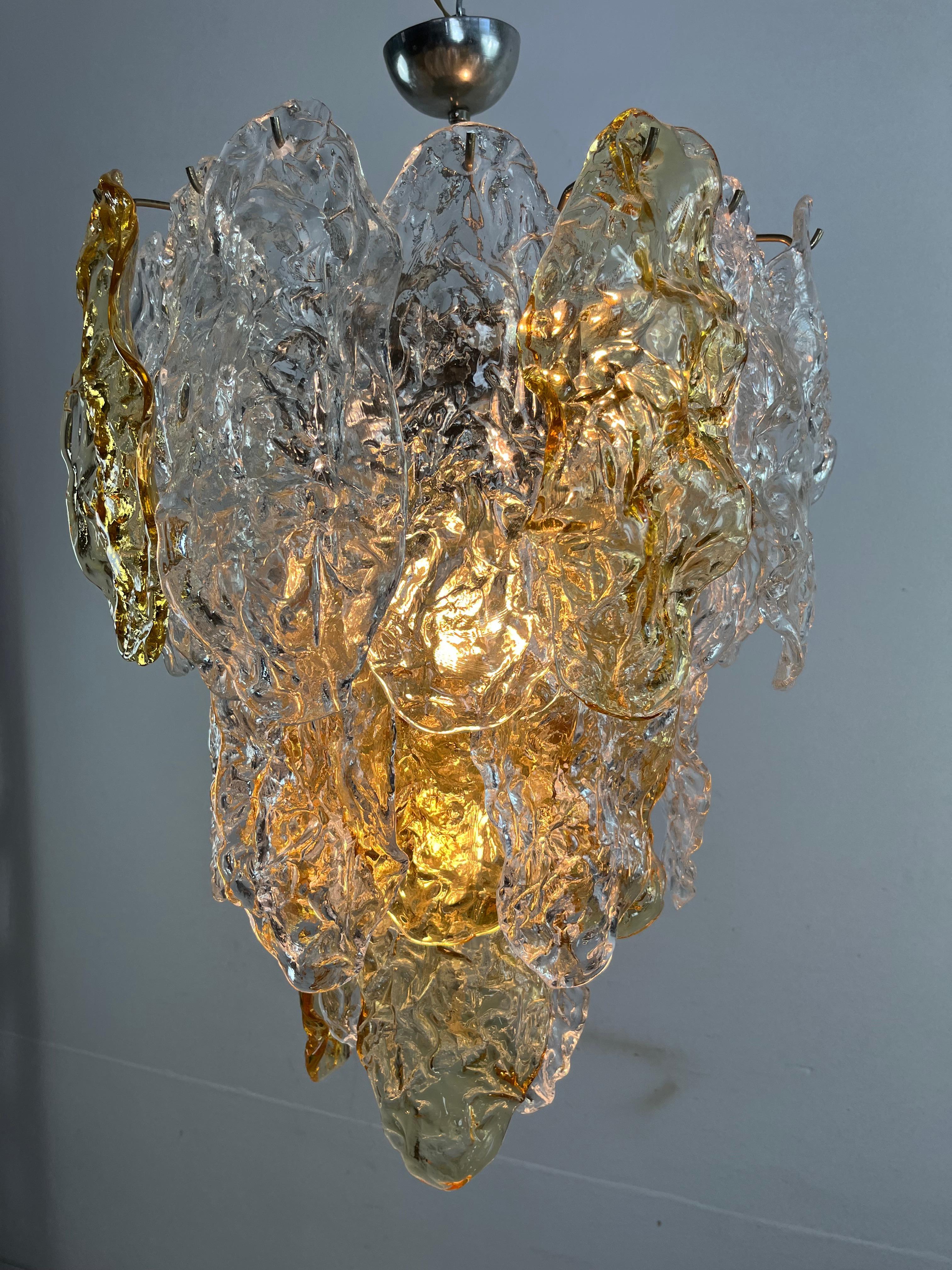 Grand lustre à 9 lumières en verre de Murano, facture d'achat de 1978,  diamètre de 50 cm et hauteur de 70 cm.
Structure métallique.
Lunettes intactes, en plus que bon état, la facture d'achat de 1978 est jointe.

Nous garantissons une expédition